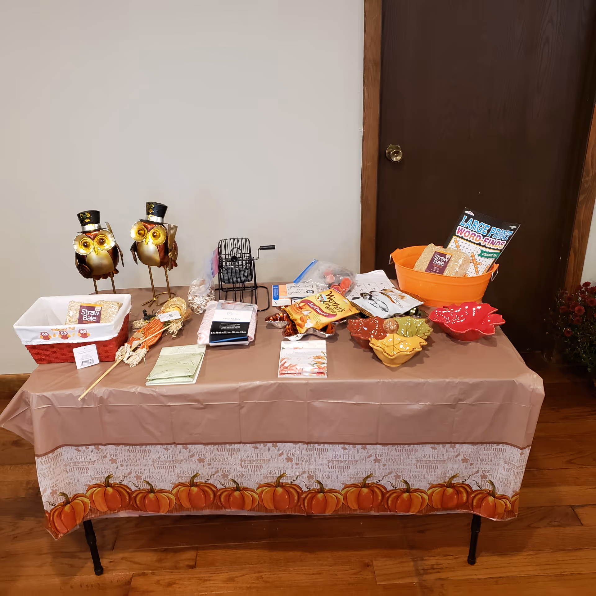 Indoor display table with pumpkin-themed cloth and assorted goodies at a care facility.