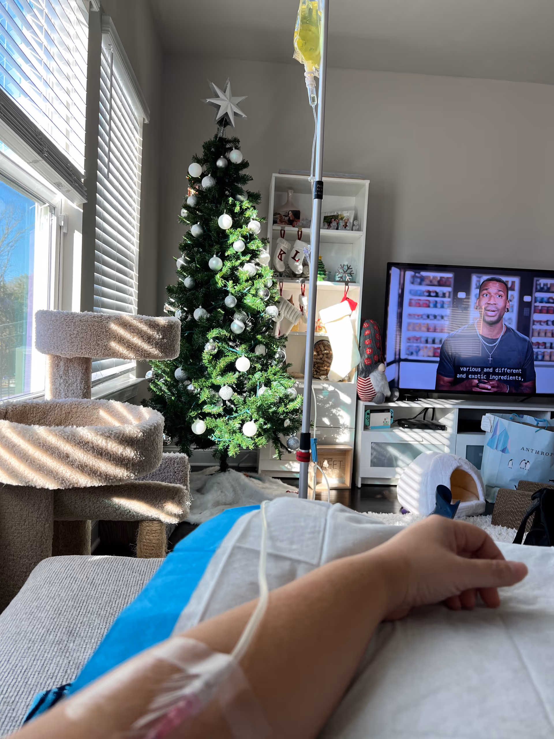 IV pole beside a decorated Christmas tree in a cozy living room with a TV.