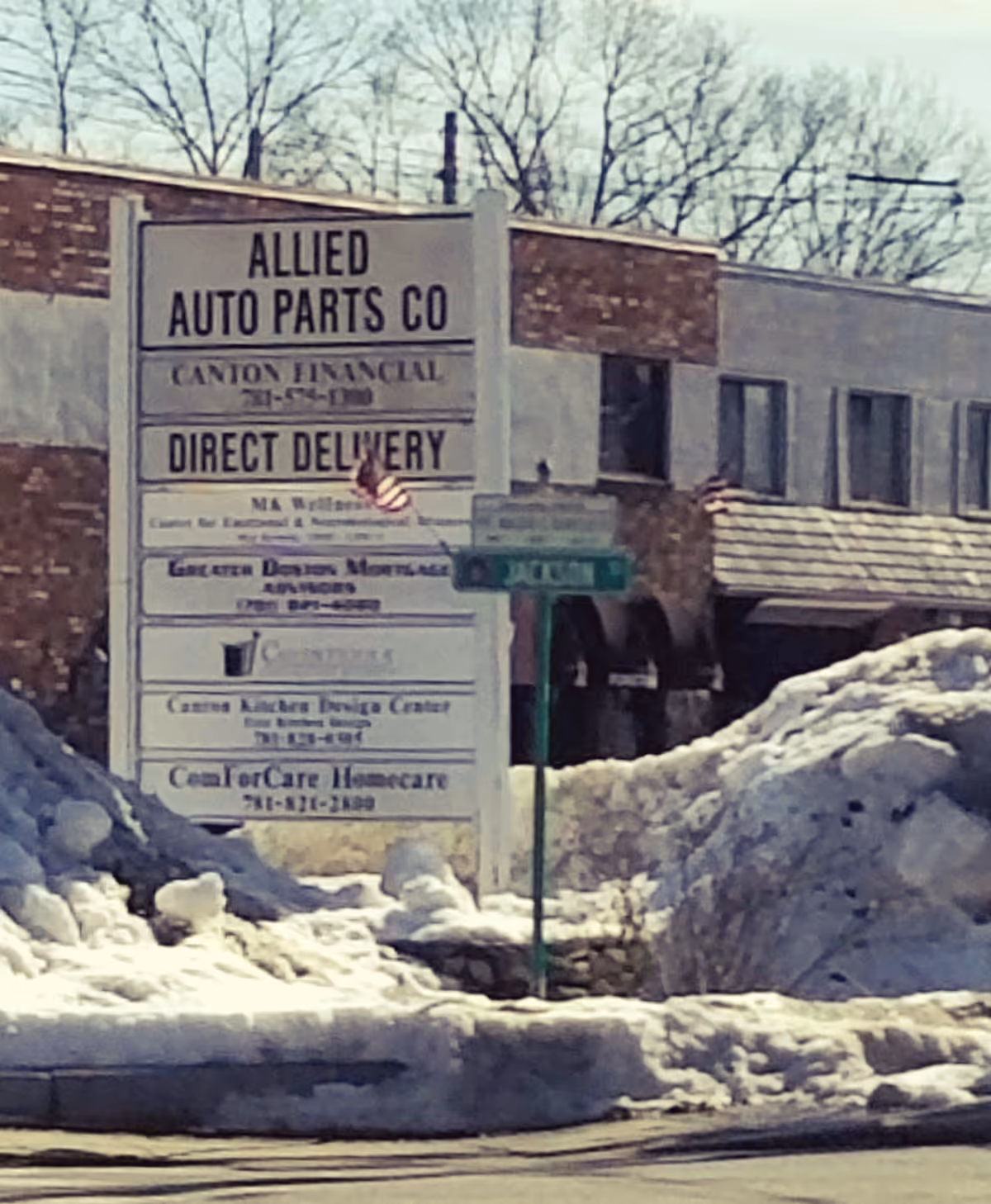 Snowy exterior signboard listing multiple businesses outside a brick building.
