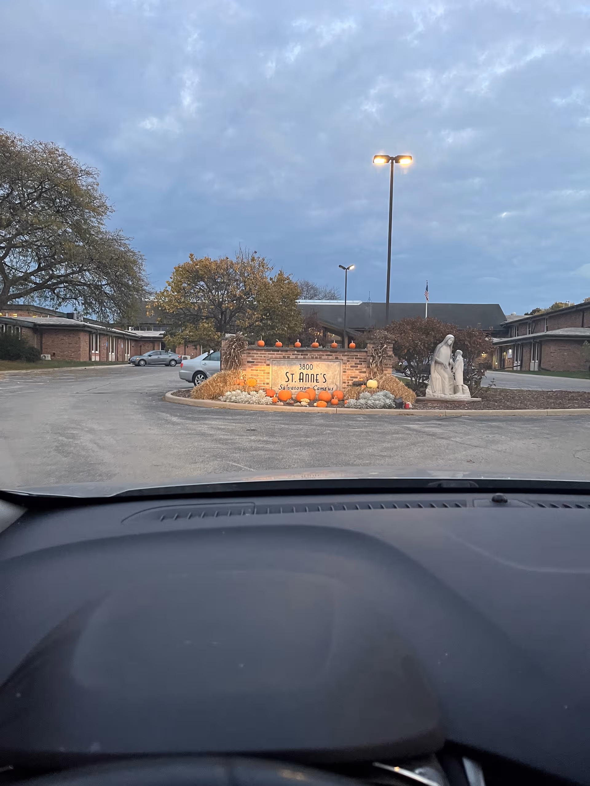 Front view of St Anne's entrance sign with pumpkins and a statue near the driveway.