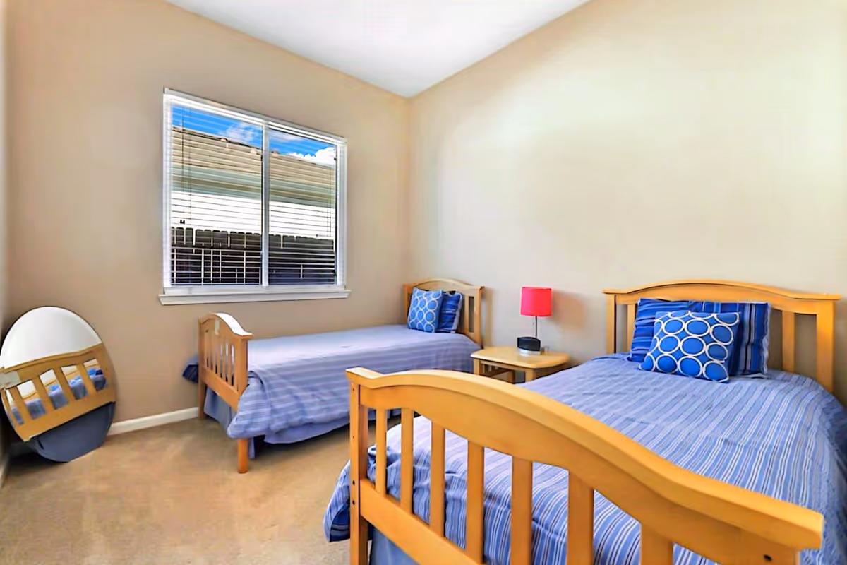 Two single beds with blue striped bedding, a window, nightstand, and mirror in a beige room.