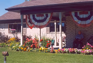 Front exterior of Cardinal Ridge Residential with brick facade, bunting, flower beds, and a resident.