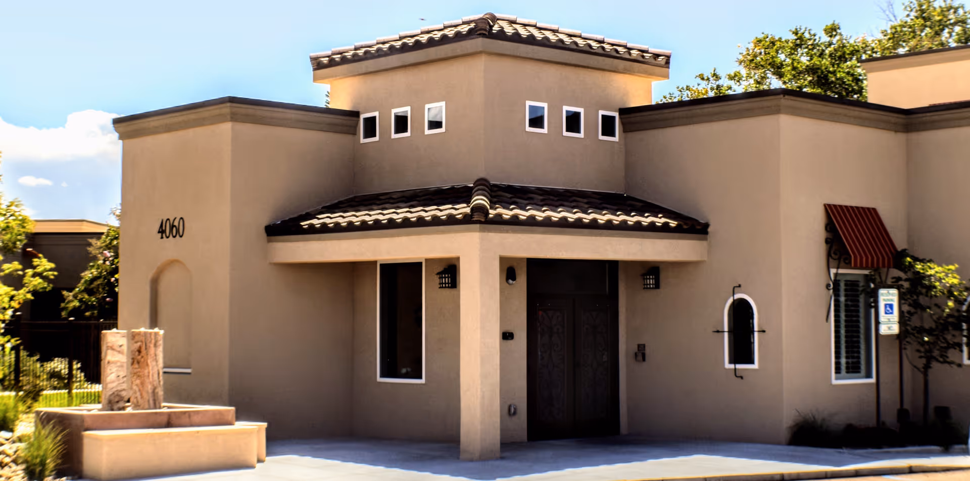 Beige stucco senior living building with tiled roof and arched entryway.