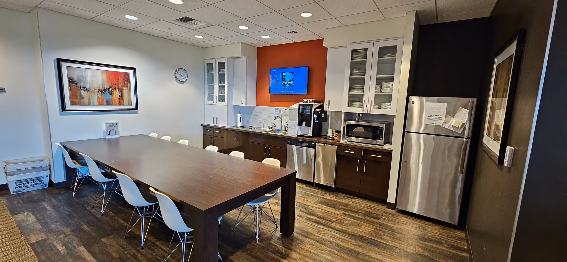 A long dining table with white chairs in a modern kitchenette area.