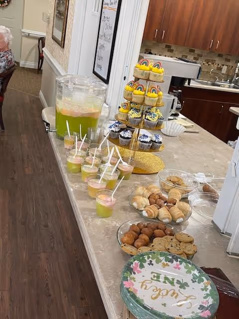 Counter with a juice dispenser, cupcakes, cookies, and pastries in a senior living facility dining area.