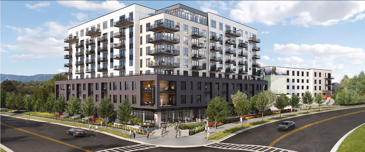 Street-level exterior view of a modern multi-story residential building with balconies, landscaped sidewalks, and cars on the road.
