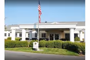 Front view of Sullivan Park Care Center with flagpole, entrance, and manicured shrubs.