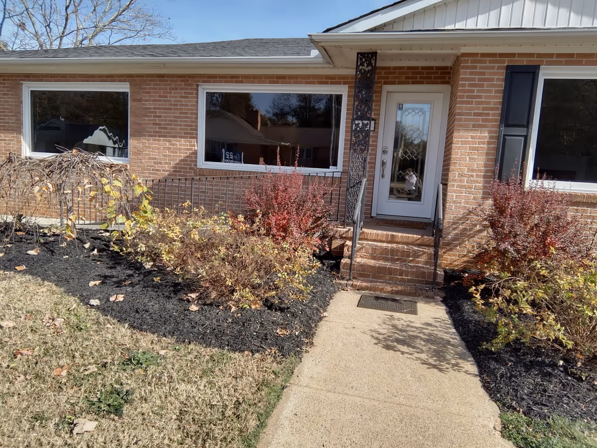 A brick senior living facility entrance with steps and landscaped shrubs.
