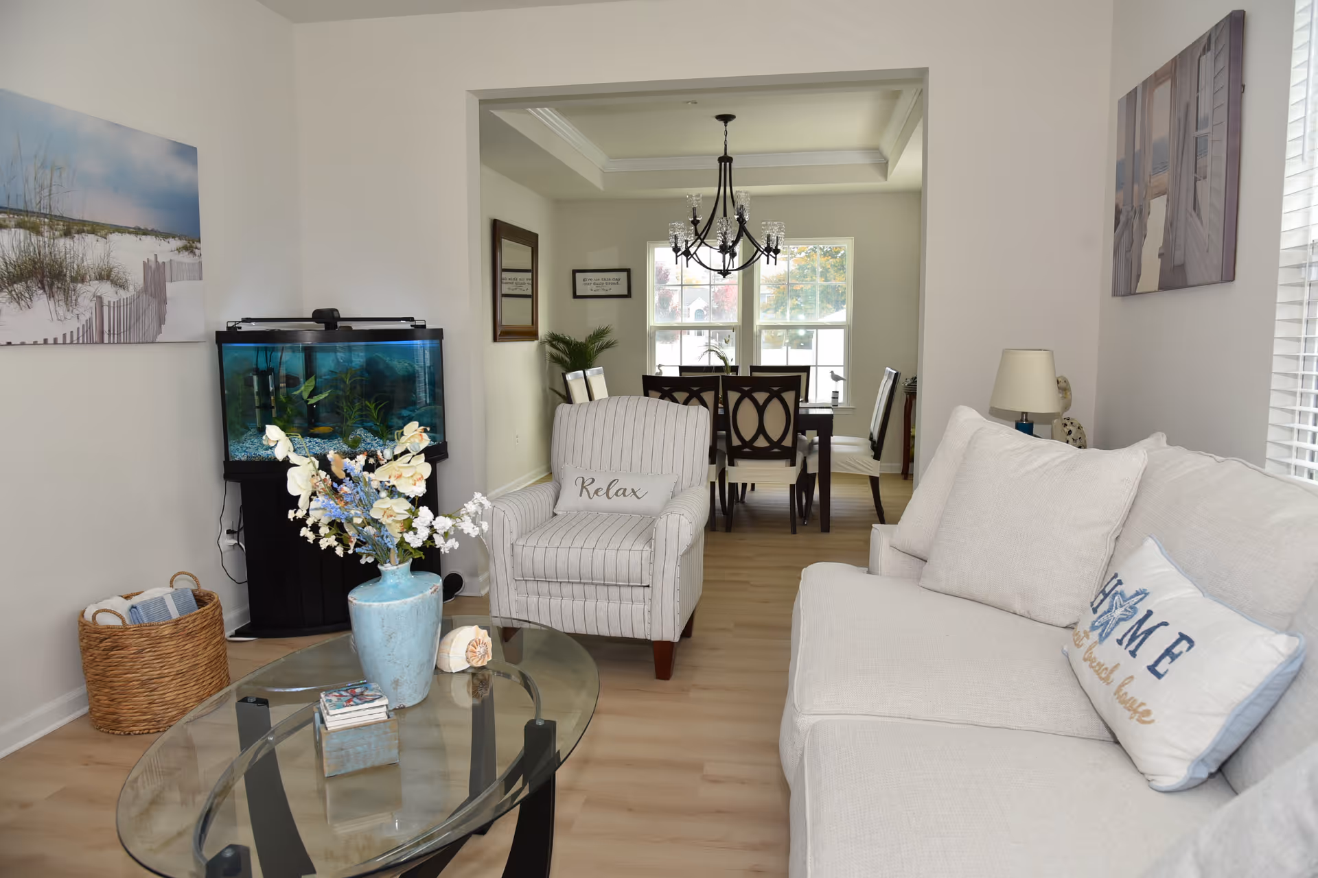Bright living room with sofa, armchair, glass coffee table, fish tank, and dining area.