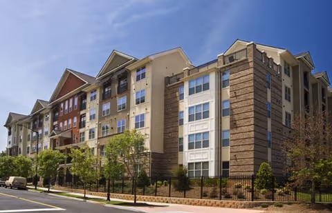 Exterior view of Oasis at Scholars Landing, a multi-story senior living building with trees.
