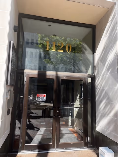 Glass entrance doors with gold number 1120 on a modern building facade.