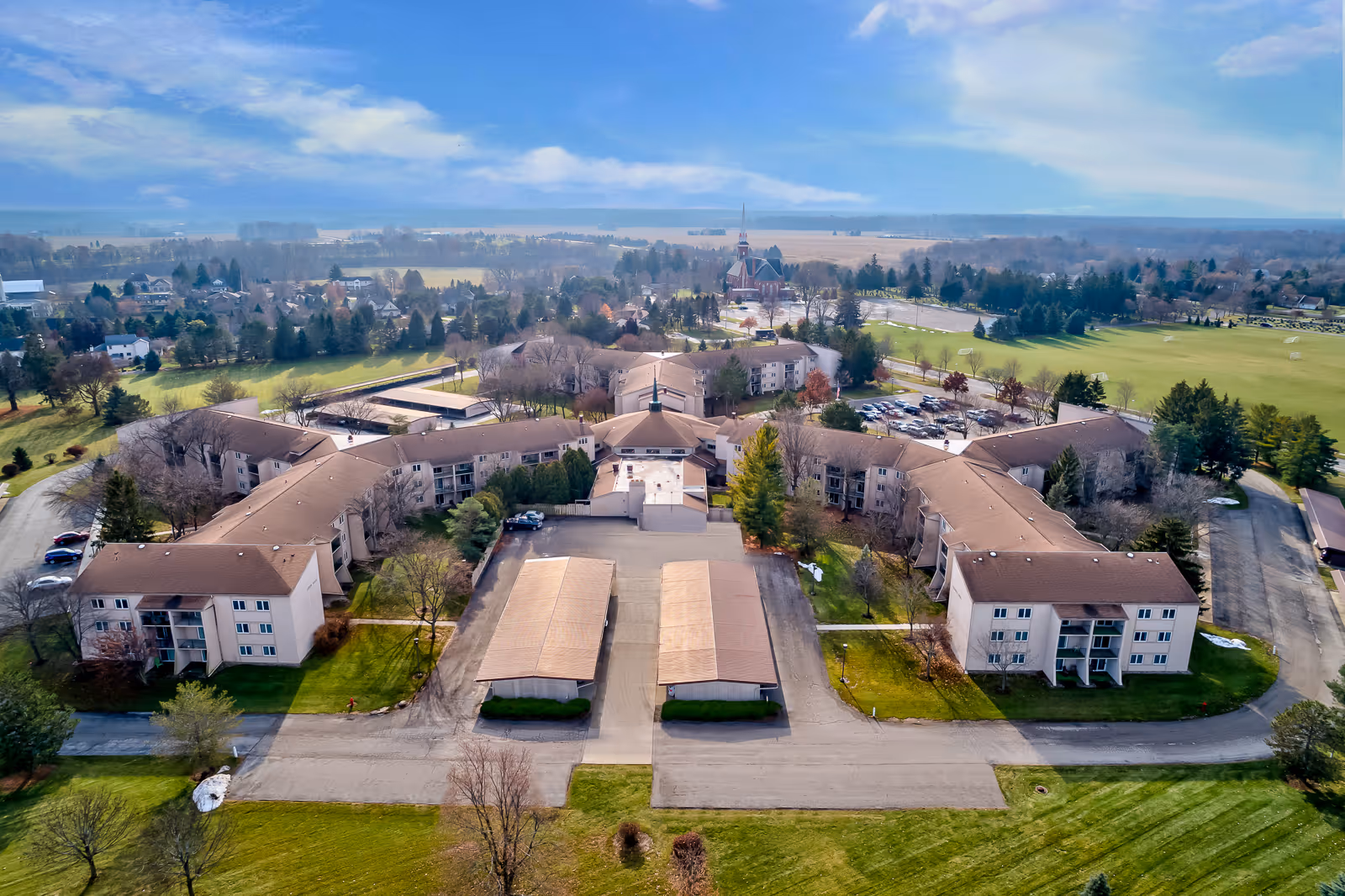 Aerial view of Holiday Winter Village campus with interconnected apartment buildings, parking areas and surrounding lawns and trees.