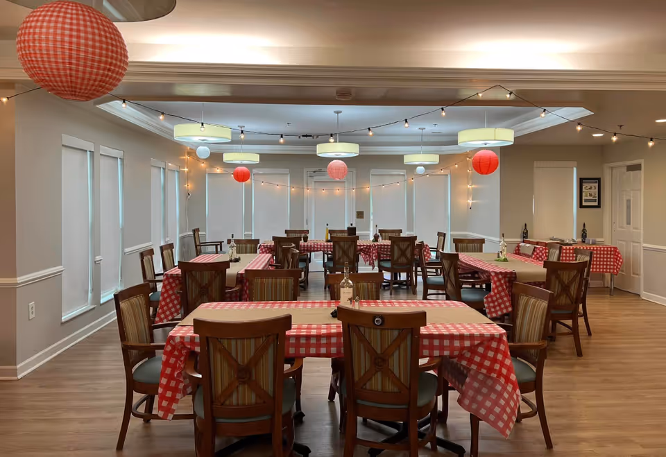 A dining room in a senior facility with red and white checkered tables and string lights.