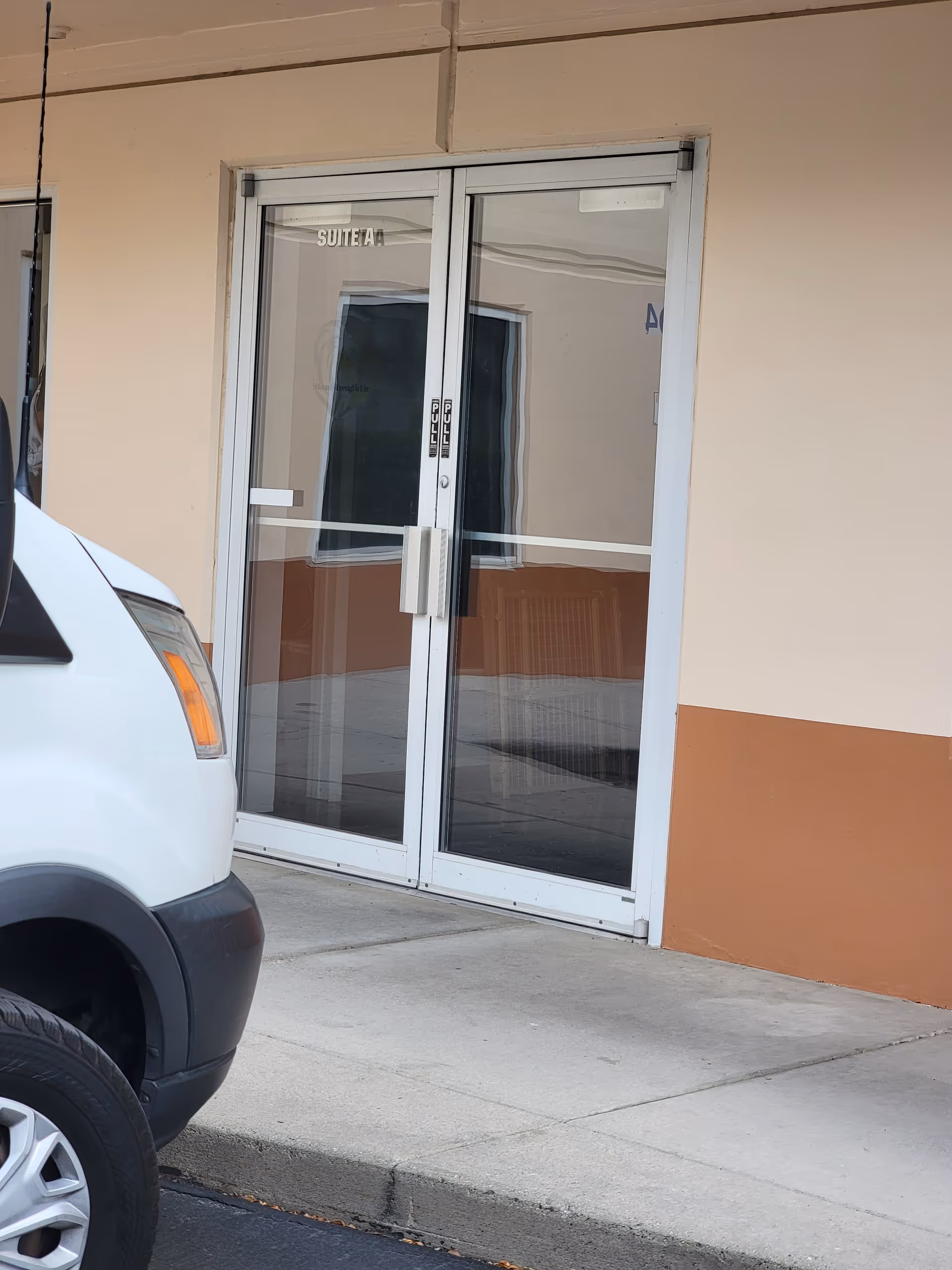 Glass double doors labeled Suite A at a beige building entrance with a parked white SUV.