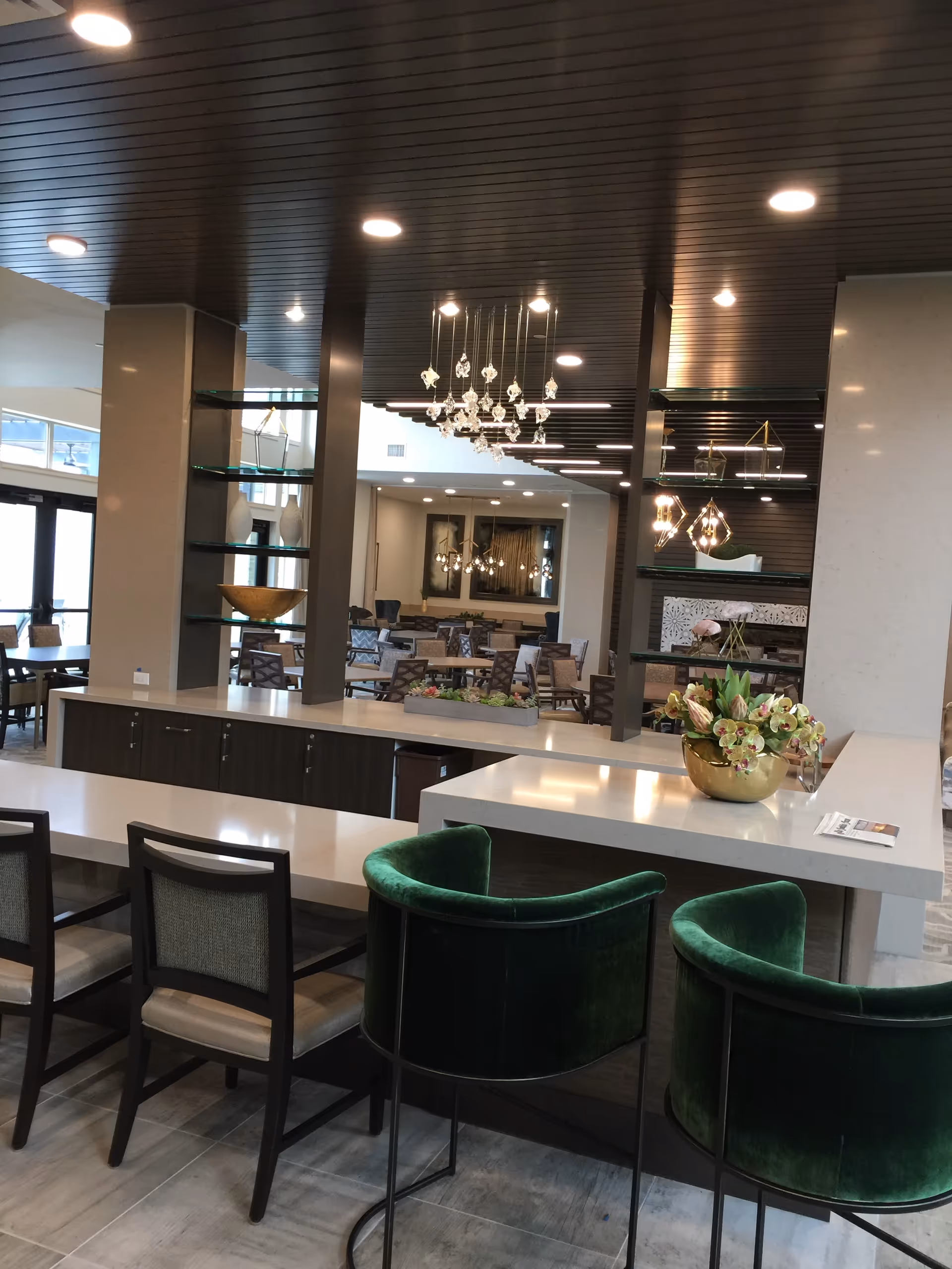 Interior view of a modern senior living dining area with green velvet chairs and chandeliers