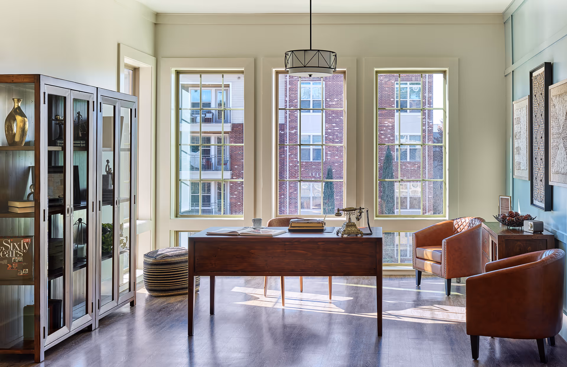 Bright modern office-like study with a wooden desk, leather chairs, shelves, and large windows.