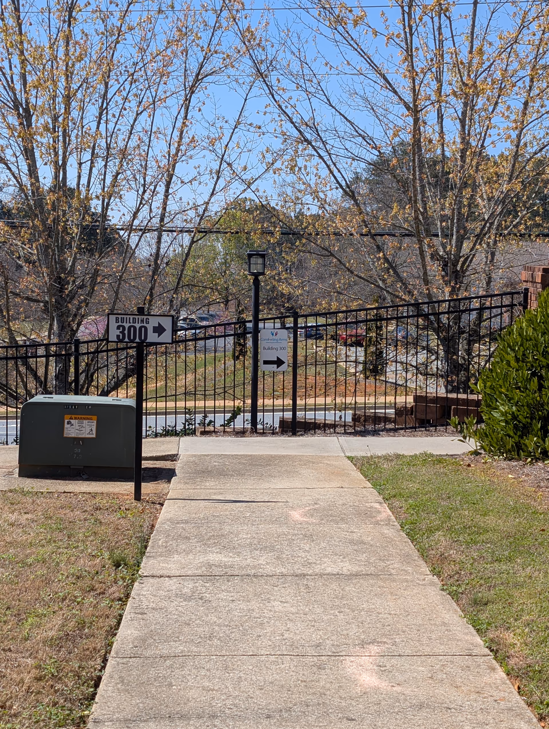 Concrete walkway leads to a gated outdoor area with signs and trees.