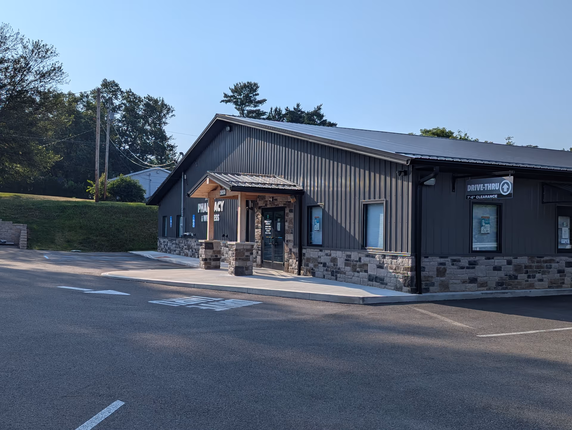 Gray metal-sided building with stone foundation and drive-thru sign, empty parking lot in foreground.