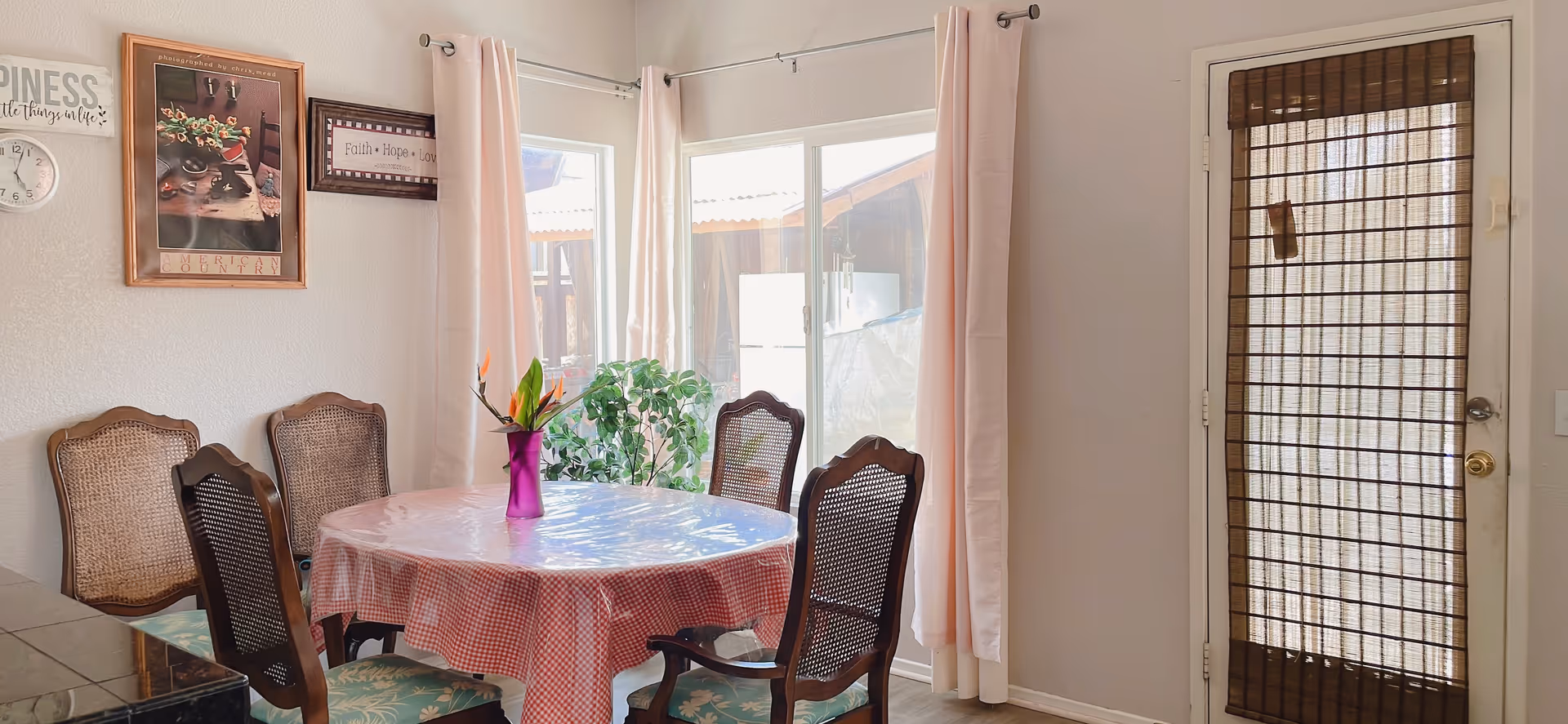 A dining room with a round table, pink tablecloth, vase, and pink curtains.