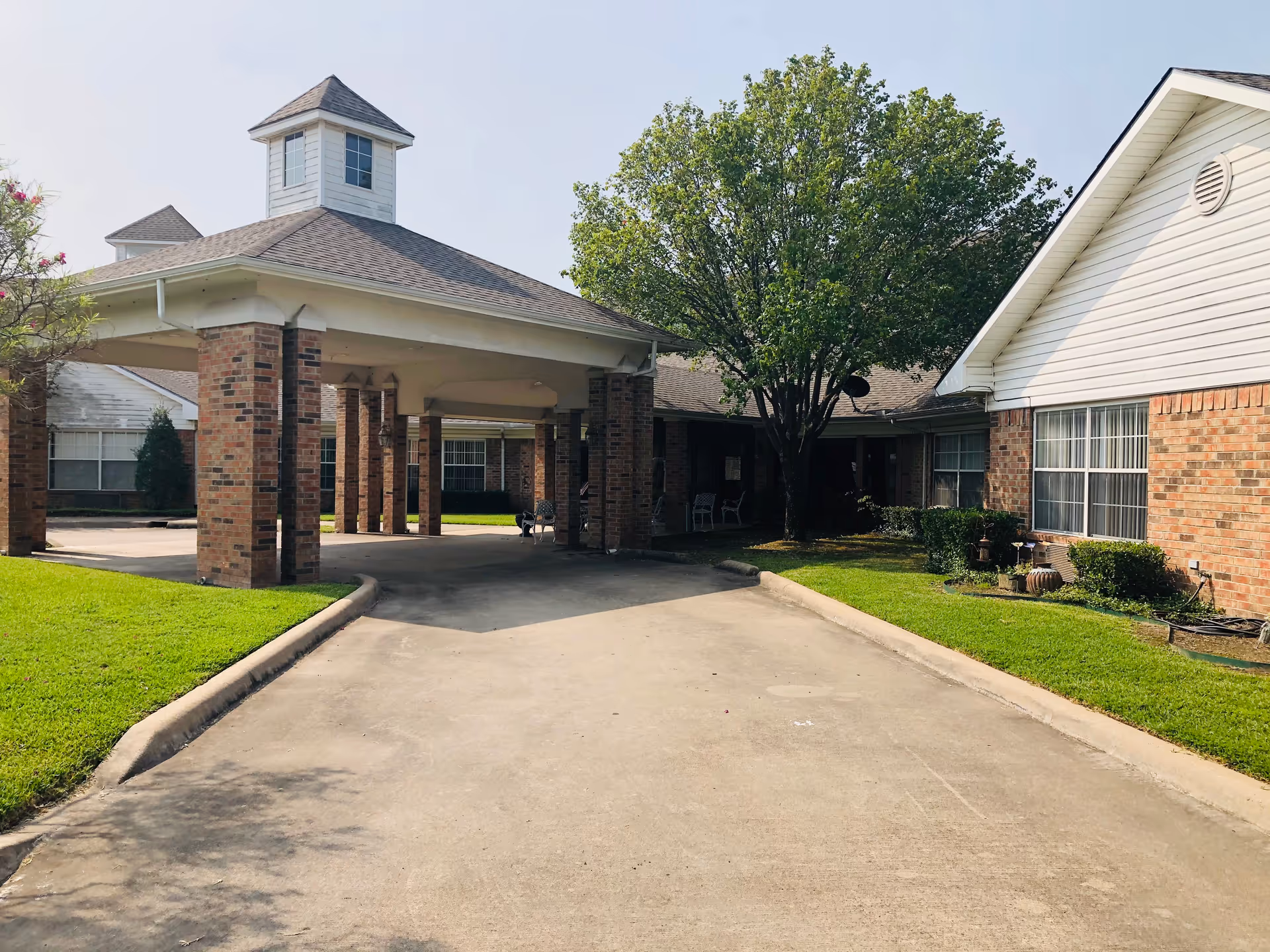 Front view of a brick assisted-living facility with a porte-cochère and landscaped grounds.
