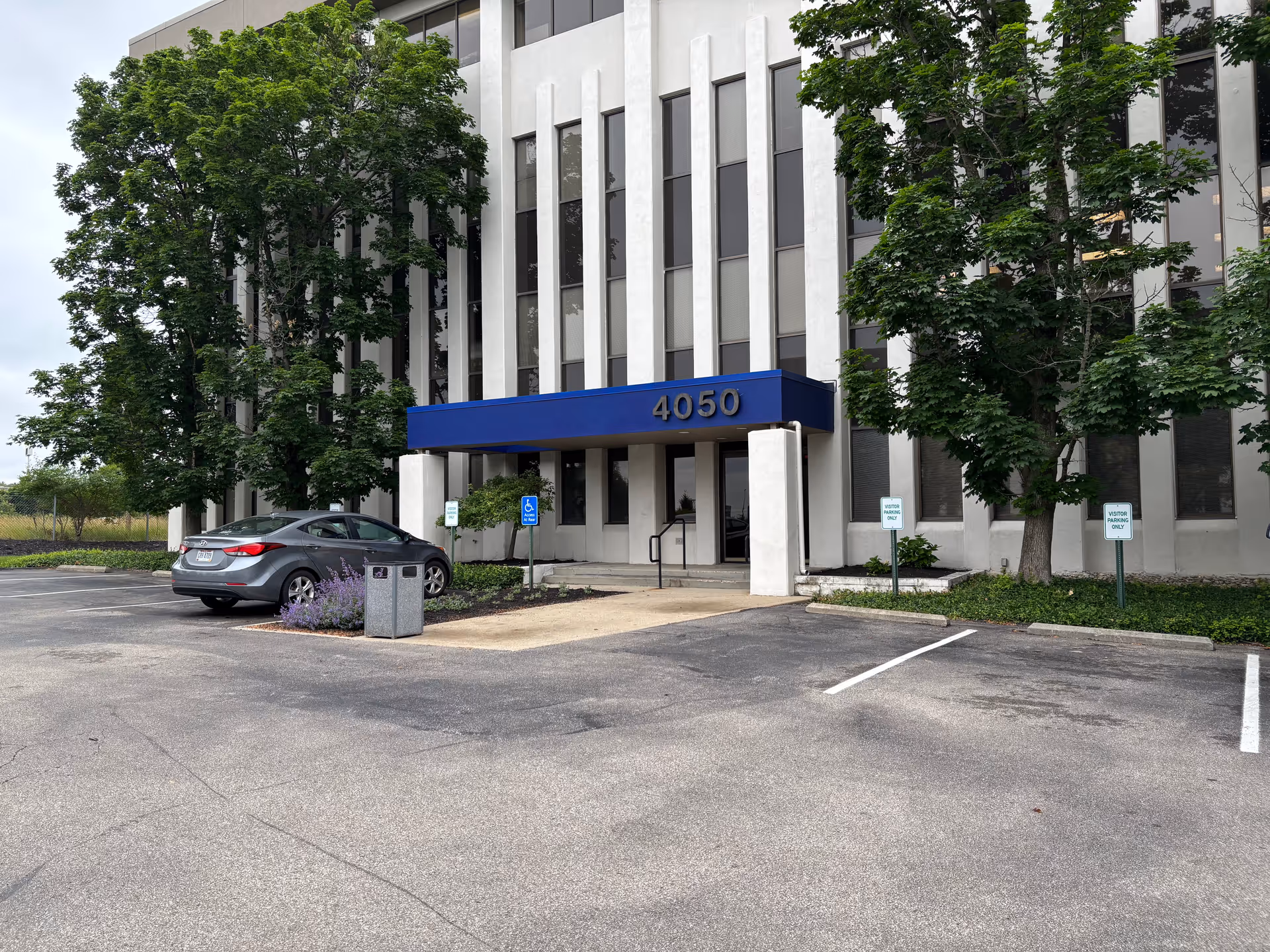 Front view of a modern building entrance with a blue canopy and parking spaces.