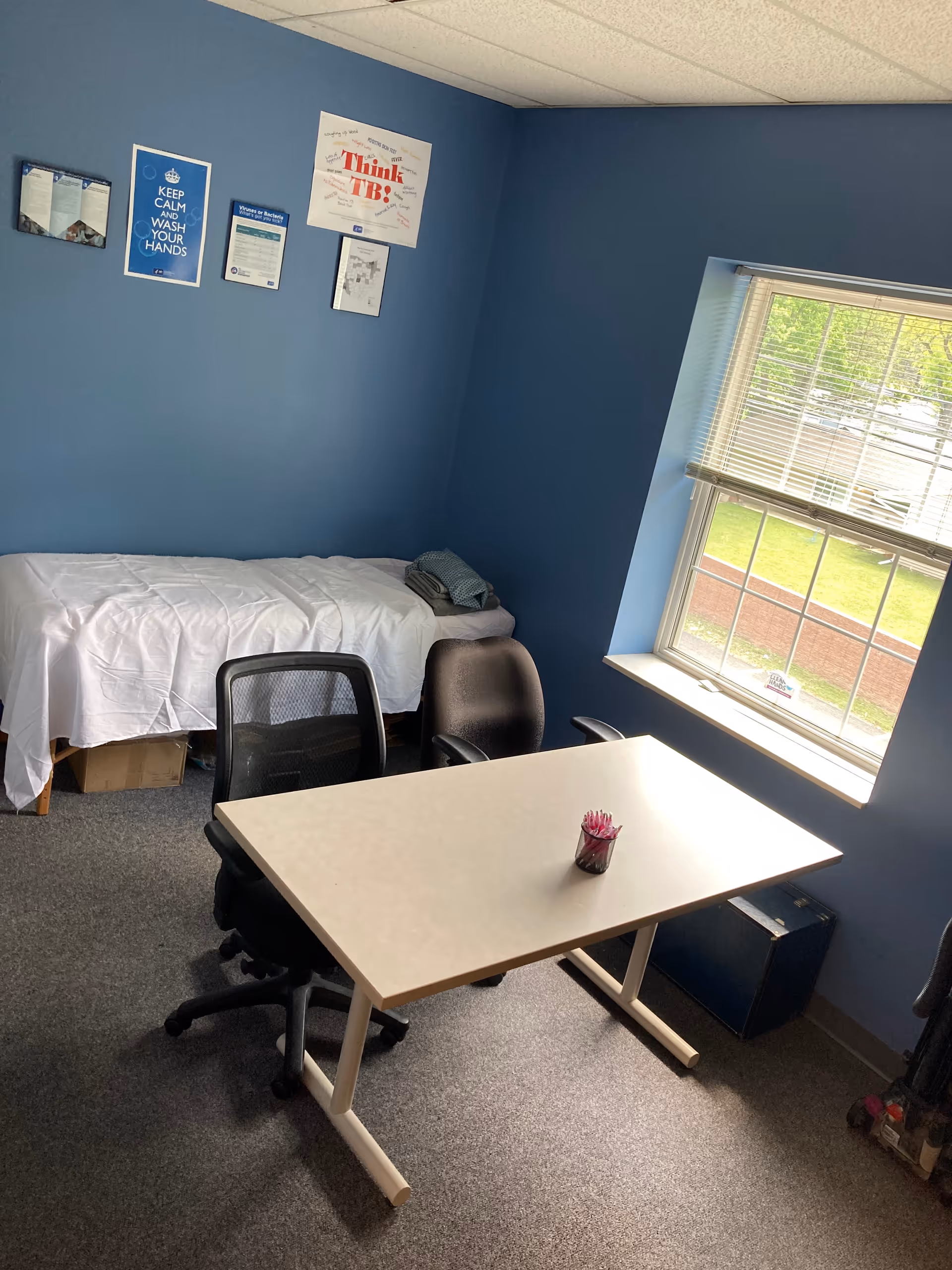 Blue-walled bedroom with a bed, desk, chairs, and daylight through the window.