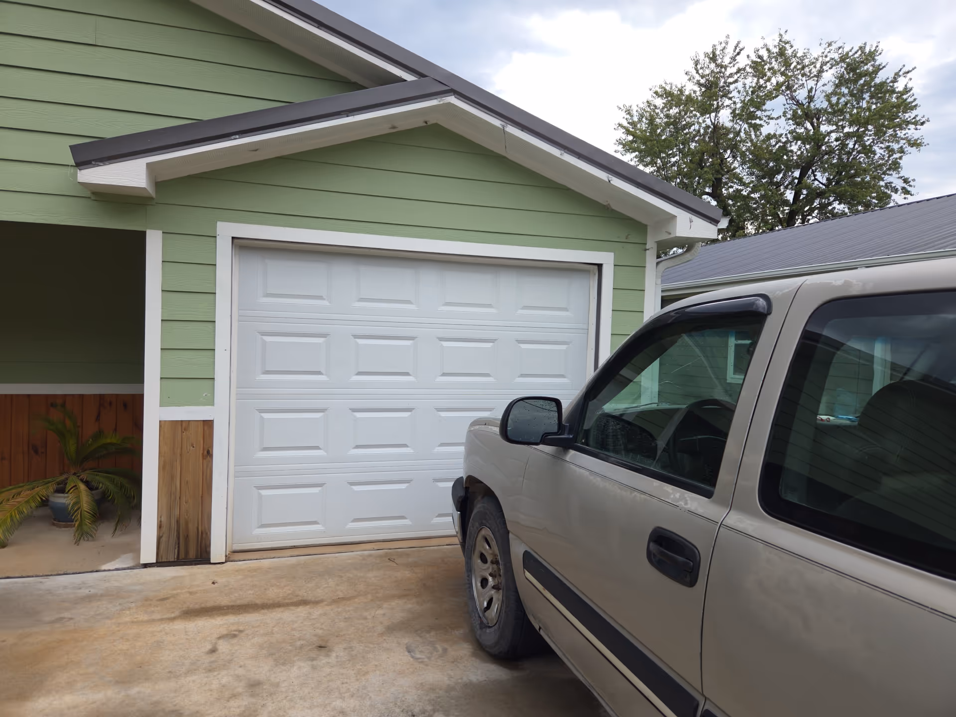 Green building with white garage door and a beige pickup truck in the driveway.