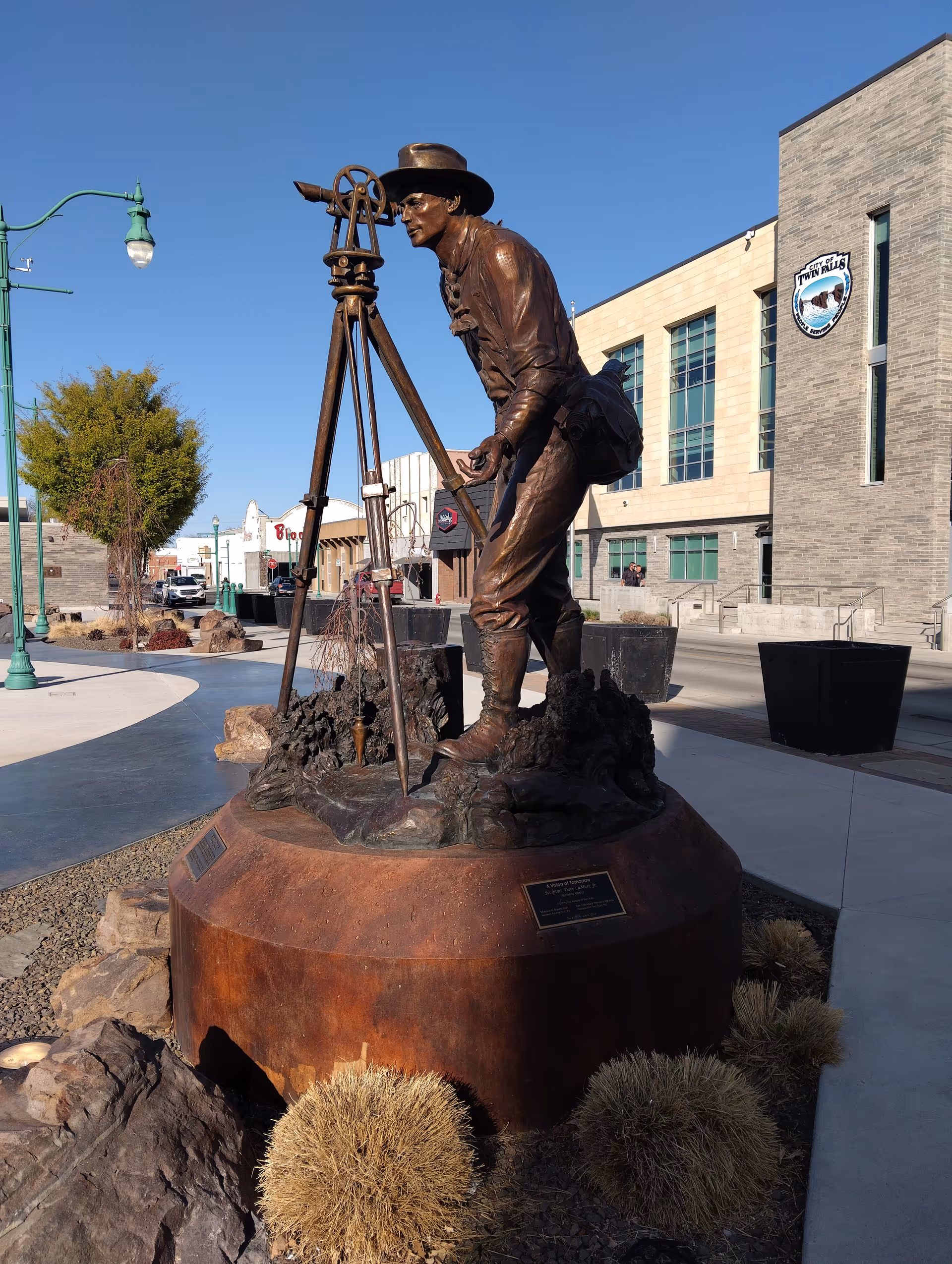 Bronze statue of a man with a camera on a tripod in an outdoor plaza.