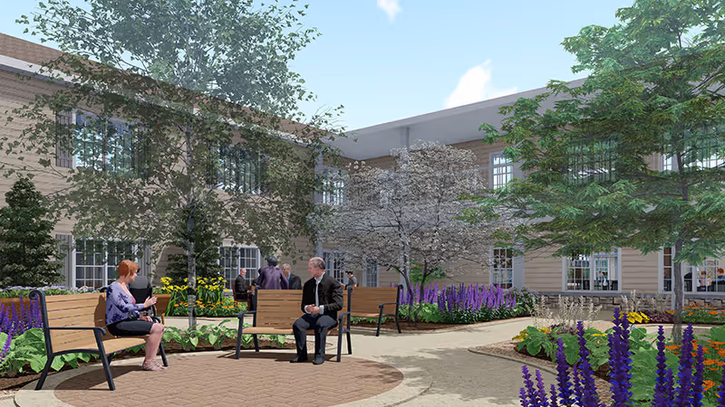 Residents sit on benches in a landscaped courtyard with flowering beds and a two-story building in the background.