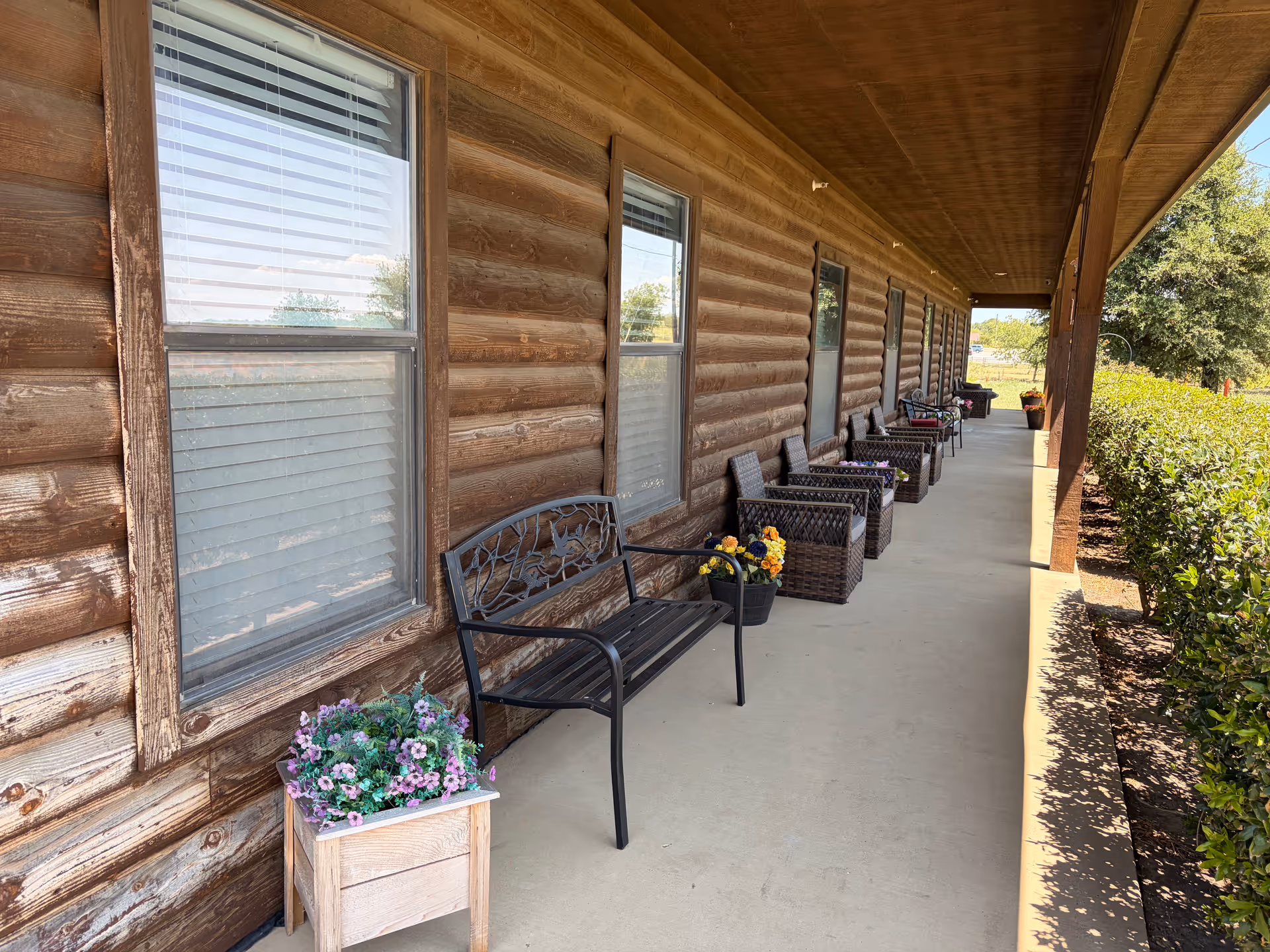 Covered exterior corridor of a rustic wooden building with outdoor chairs and potted flowers.