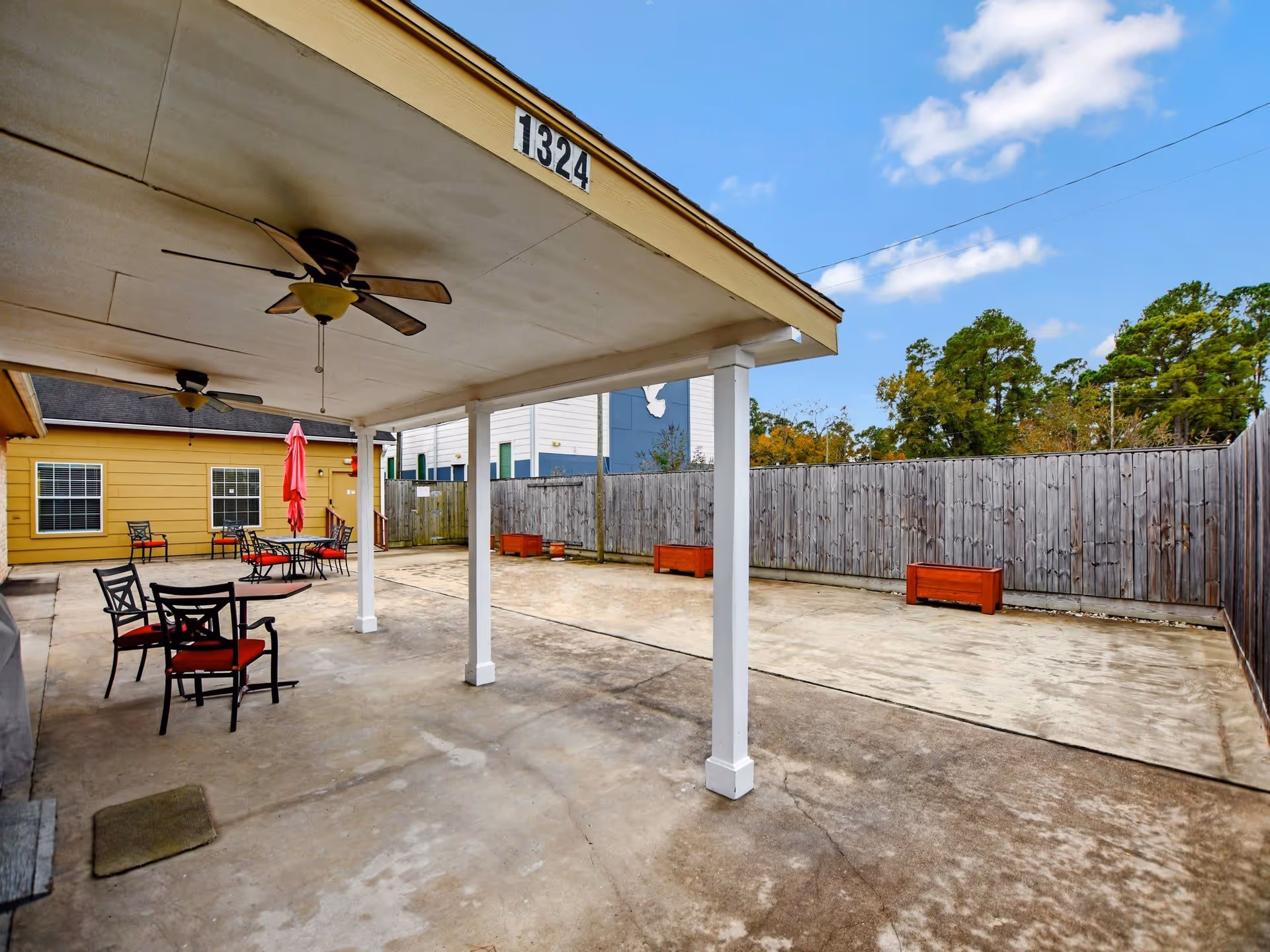 Covered outdoor patio with tables, chairs, ceiling fans and a fenced concrete courtyard.