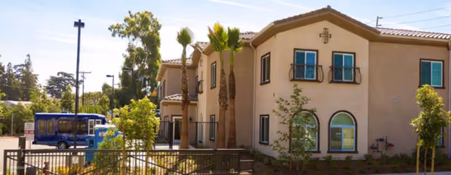 Exterior view of Silverado Brea Memory Care Community building with palm trees and a blue bus.