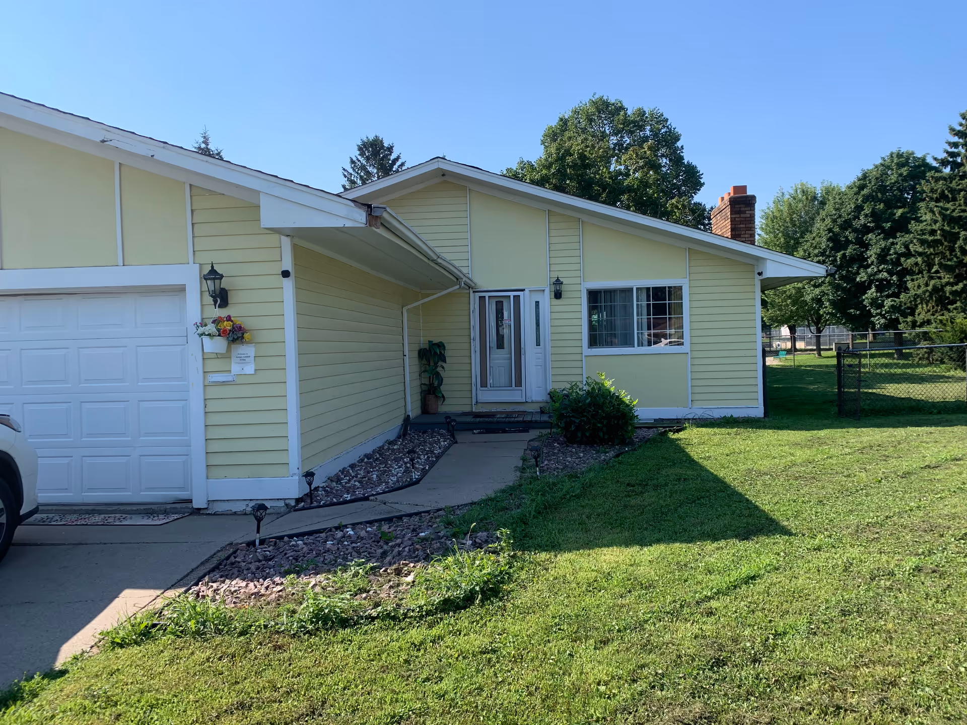 Aurora Assisted Living exterior: yellow, single-story building with front entrance, driveway, and lawn.