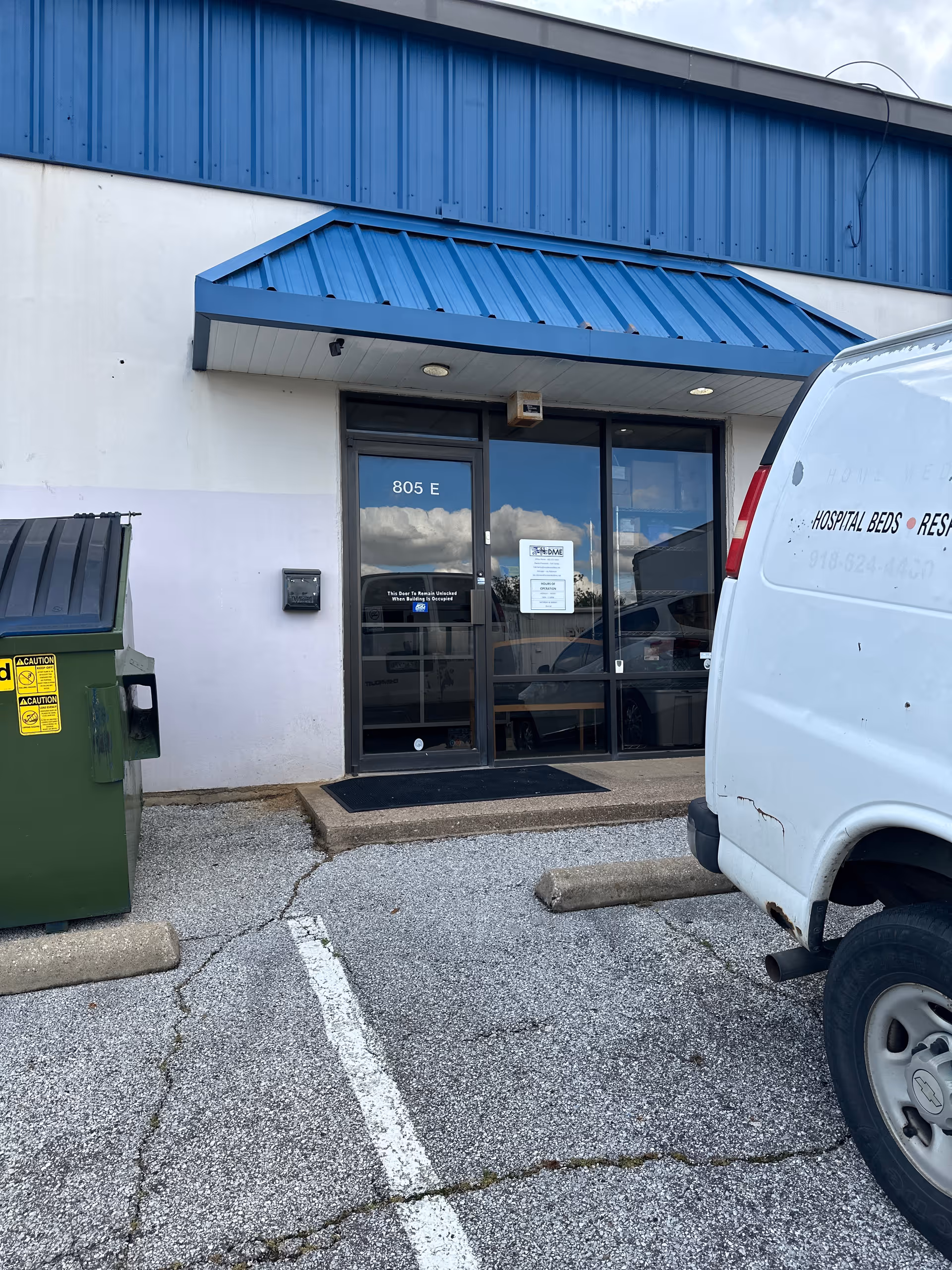 Exterior view of a medical supply facility entrance with a blue awning and a parked van.