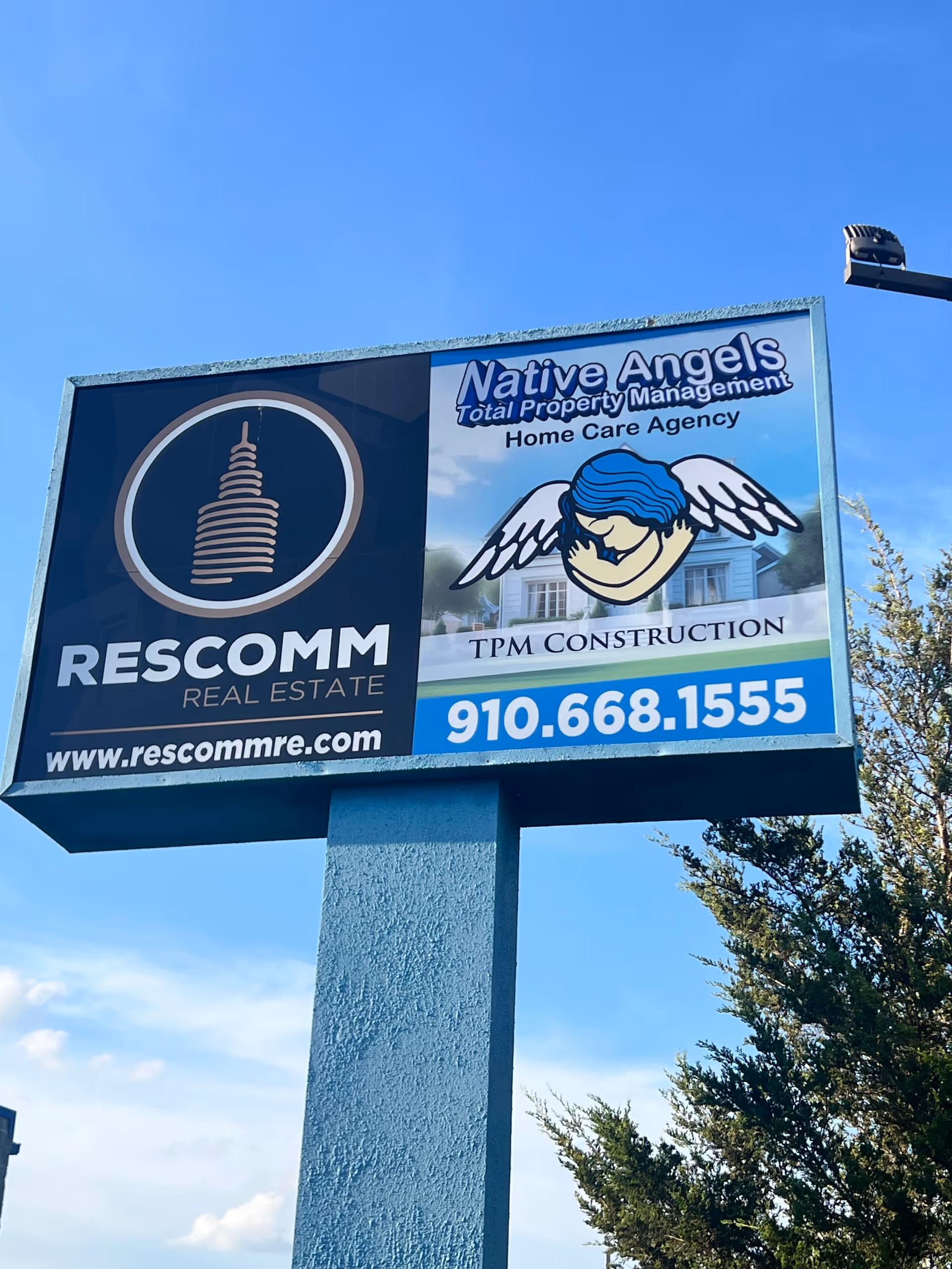 Large outdoor sign on a blue post advertising Native Angels and RESCOMM Real Estate.