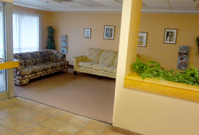 Cozy senior living lounge with floral couches, framed art, plants, and a tiled entrance.