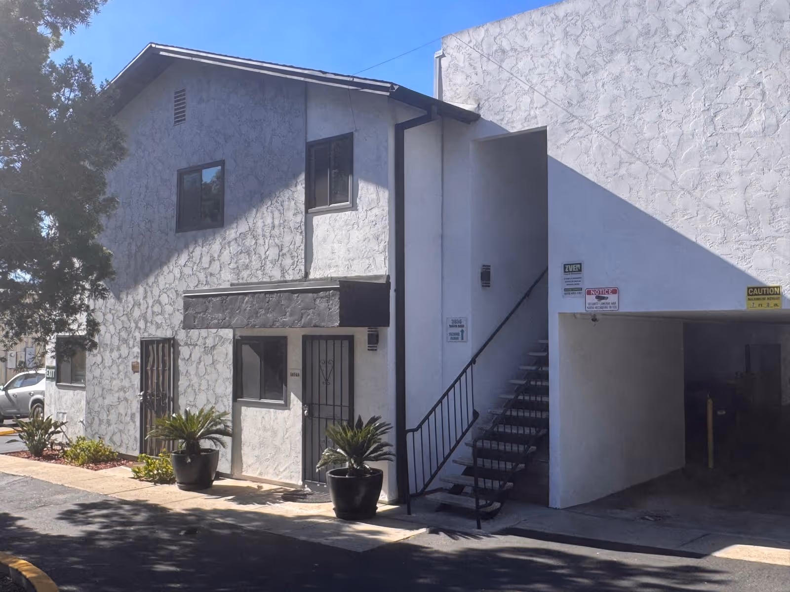 White textured building exterior with a metal staircase and potted plants by the entrance