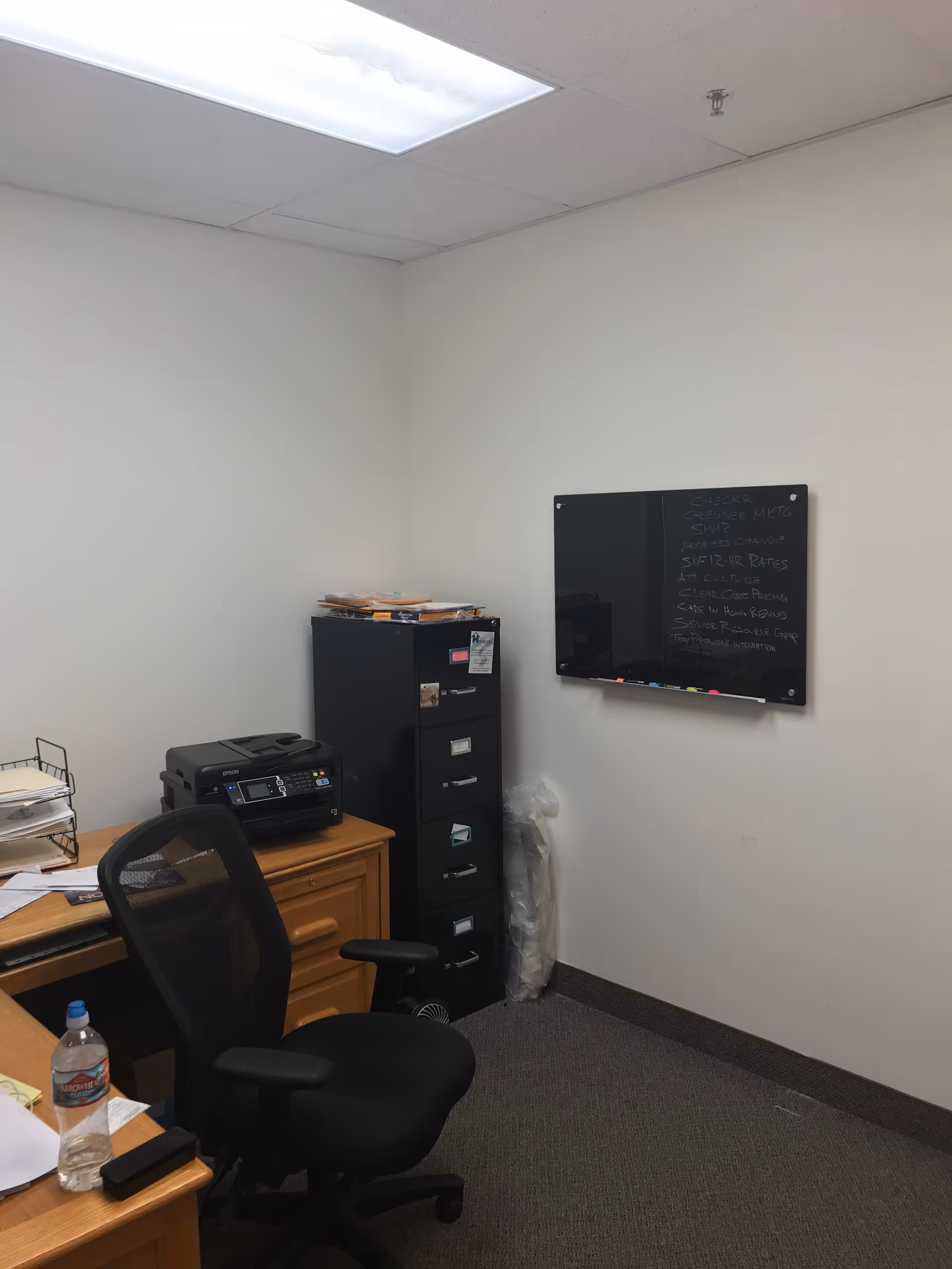 Office corner with desk, chair, printer, filing cabinet, and a blackboard on the wall.