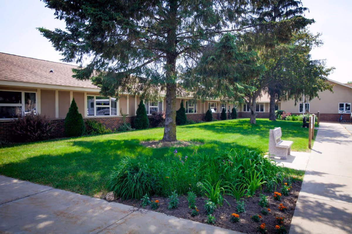 Exterior view of Onalaska Care Center with lawn, trees, and a bench.