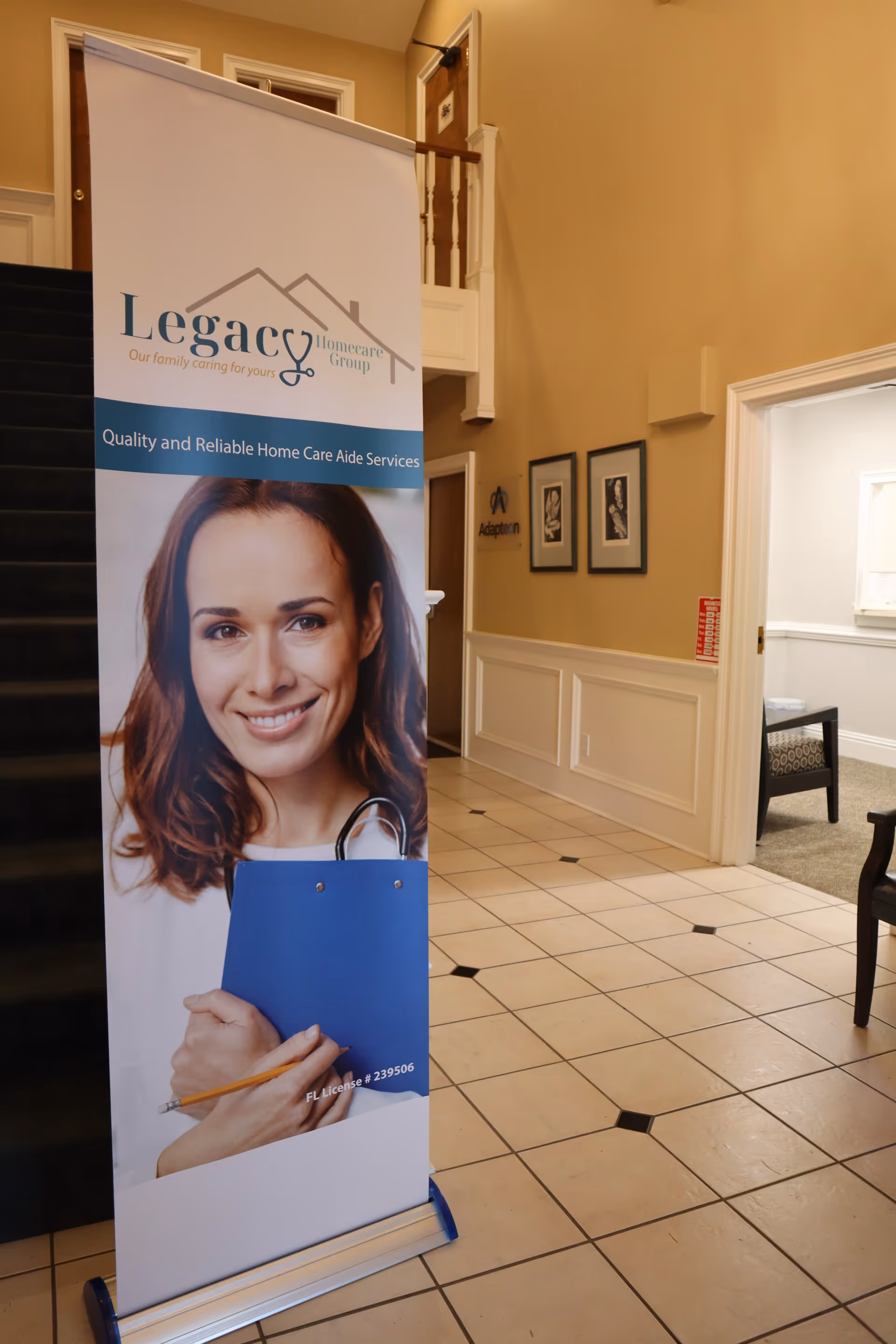 Indoor lobby featuring a Legacy Homecare Group banner, tiled floor, staircase, and framed photos.