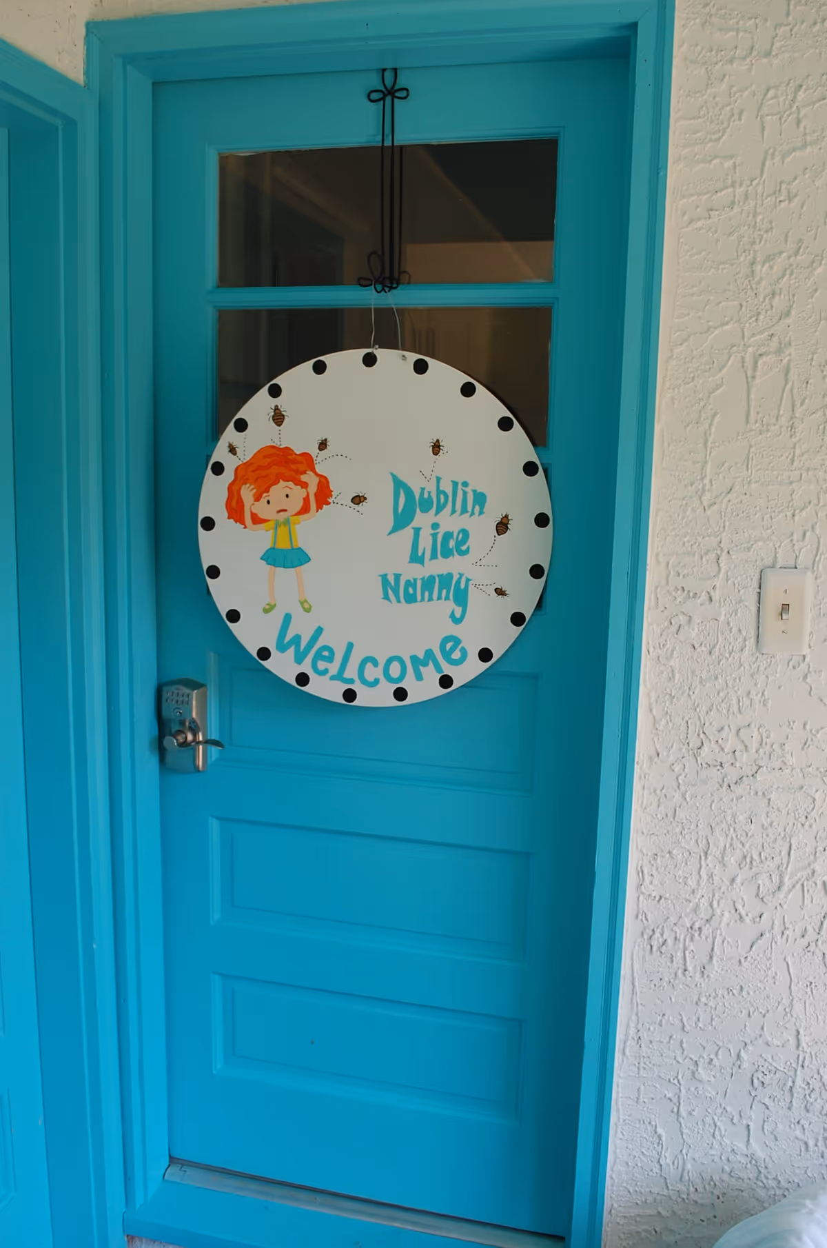 Bright turquoise front door with a round Welcome sign featuring a cartoon girl.