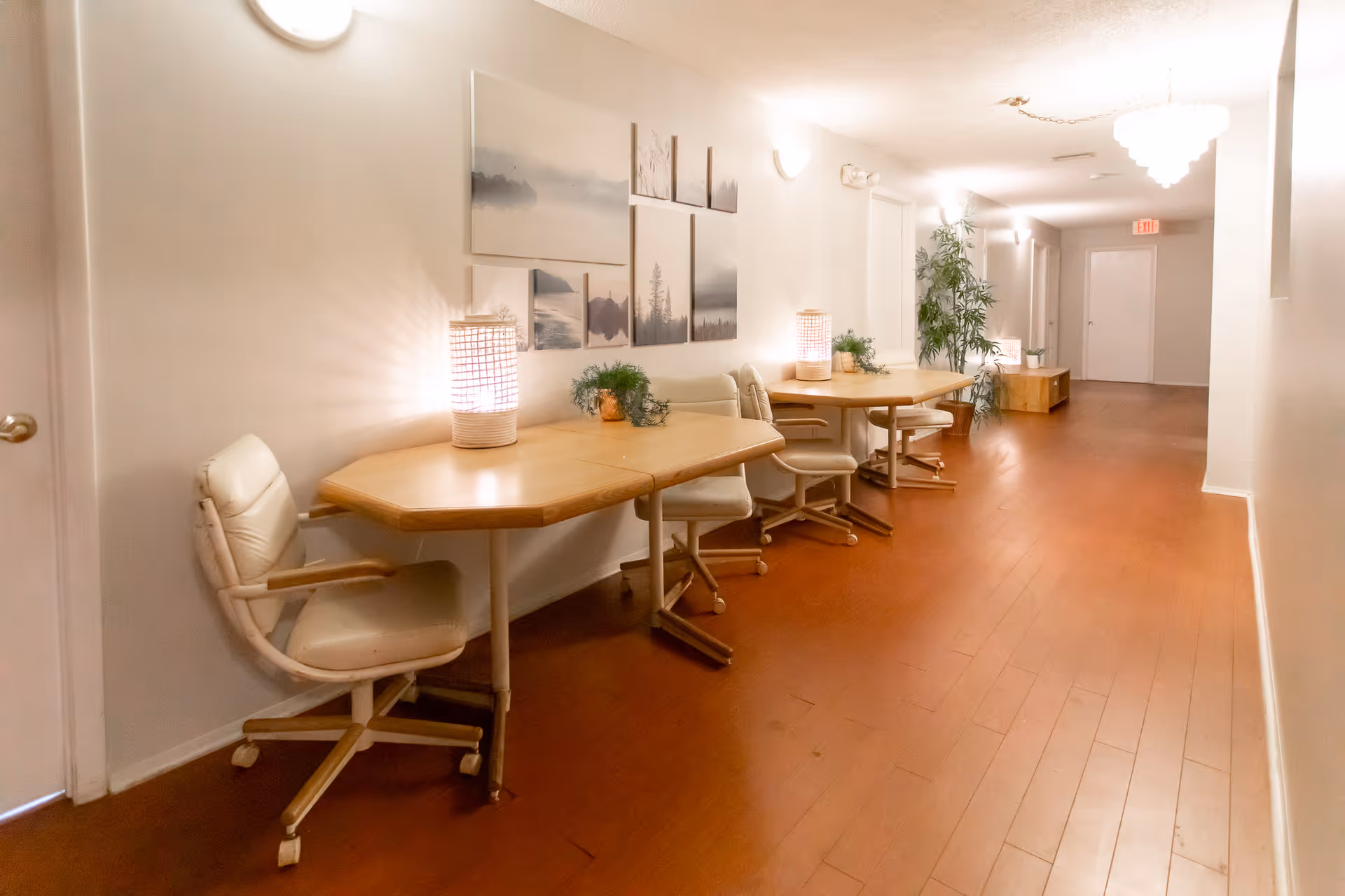 Long hallway with wooden floors, tables, white chairs, lamps, and wall art.