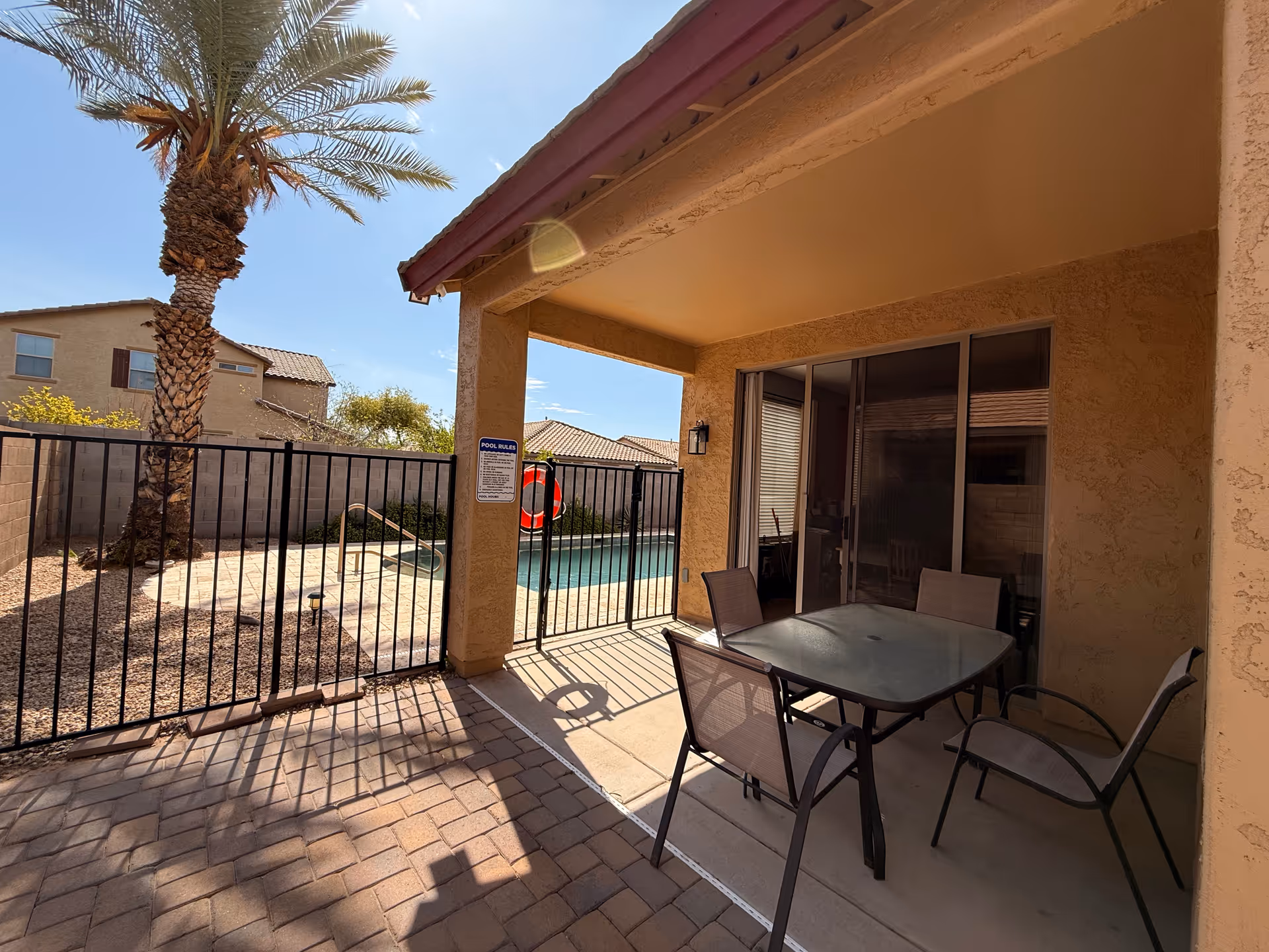 Outdoor patio with table and chairs, pool visible beyond a black fence.