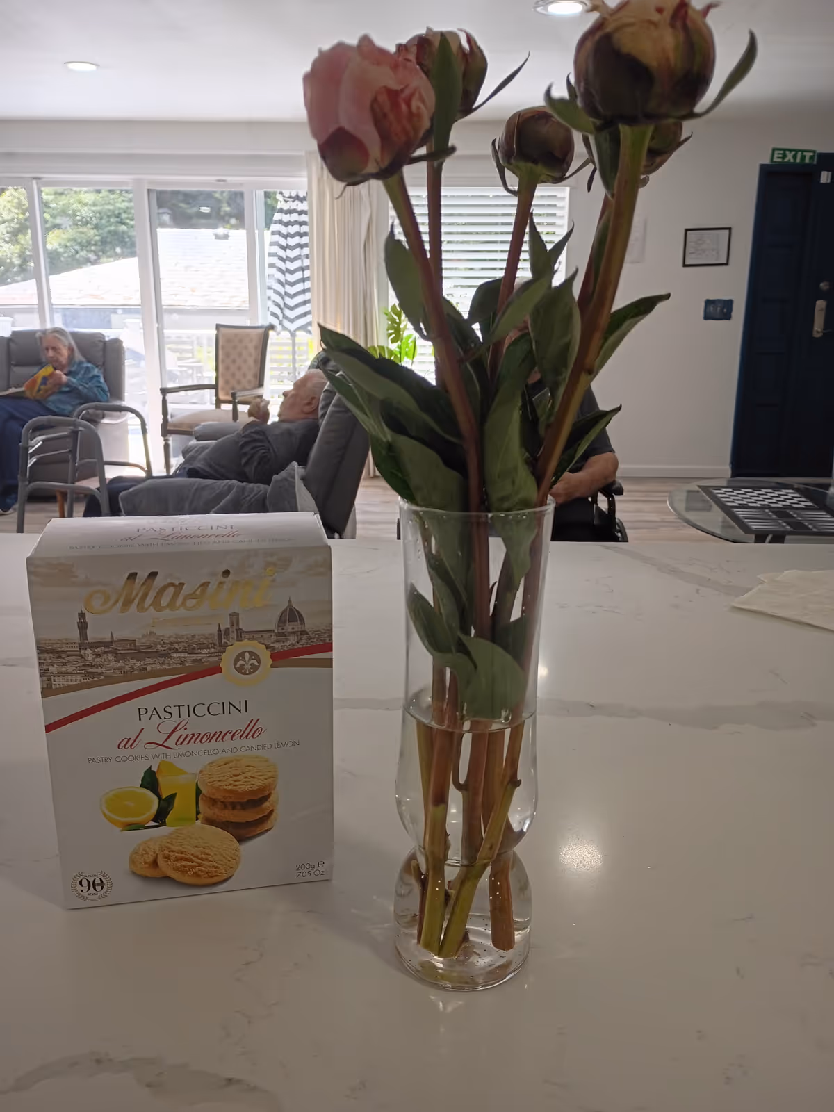 Vase of pink flowers and a cookie box on a counter in a bright living room.