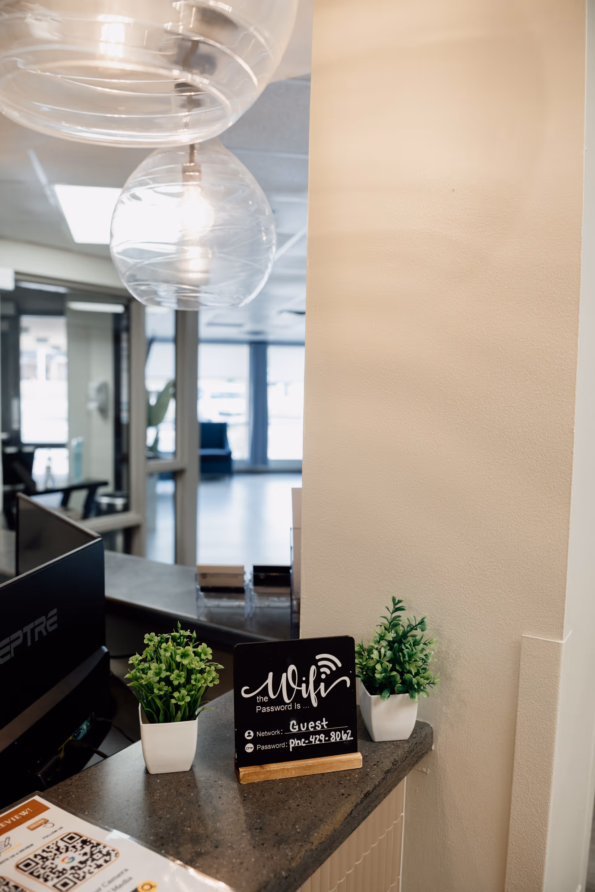 Reception area with two potted plants, a chalk WiFi sign, and glass pendant lights.