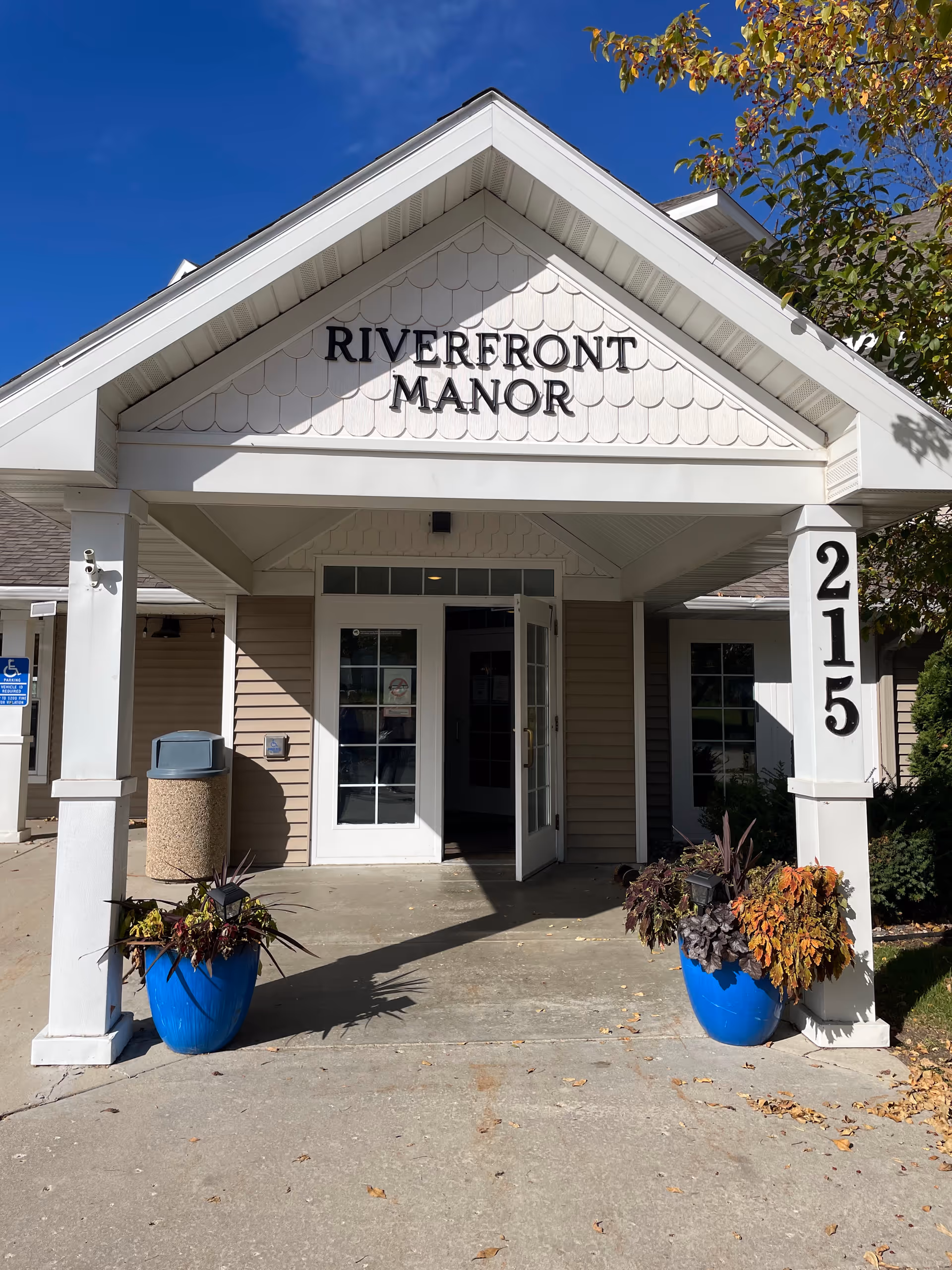 Riverfront Manor front entrance with white columns, peaked roof, and blue planters.