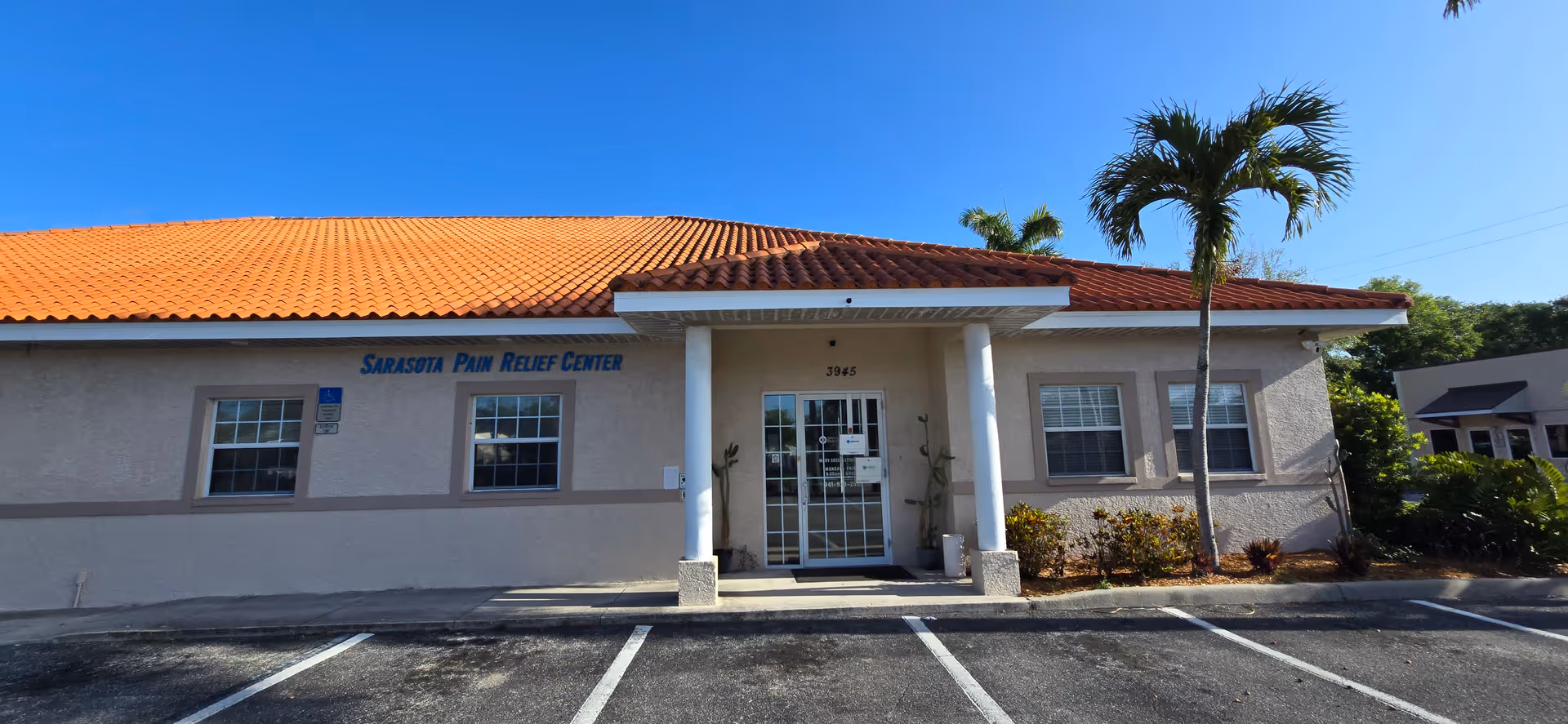 Exterior view of Sarasota Pain Relief Center building with entrance, parking lot, and palm trees.