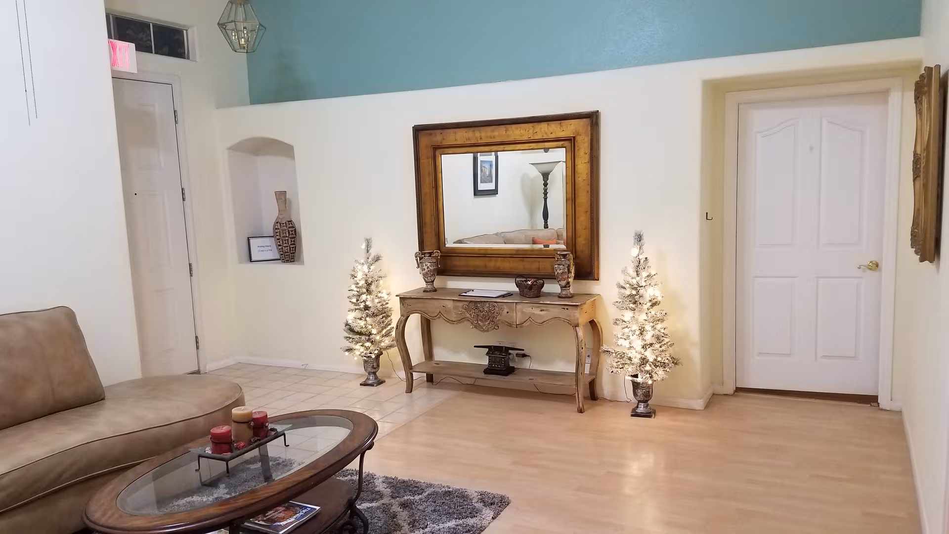 Cozy living room with sofa, glass coffee table, console table with mirror, and lit decorative trees.