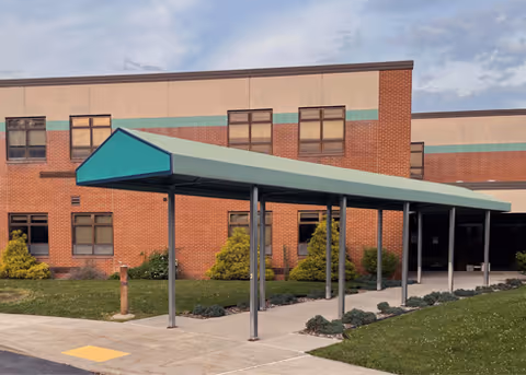 Brick senior living facility with a teal canopy over the entrance and landscaped shrubs.