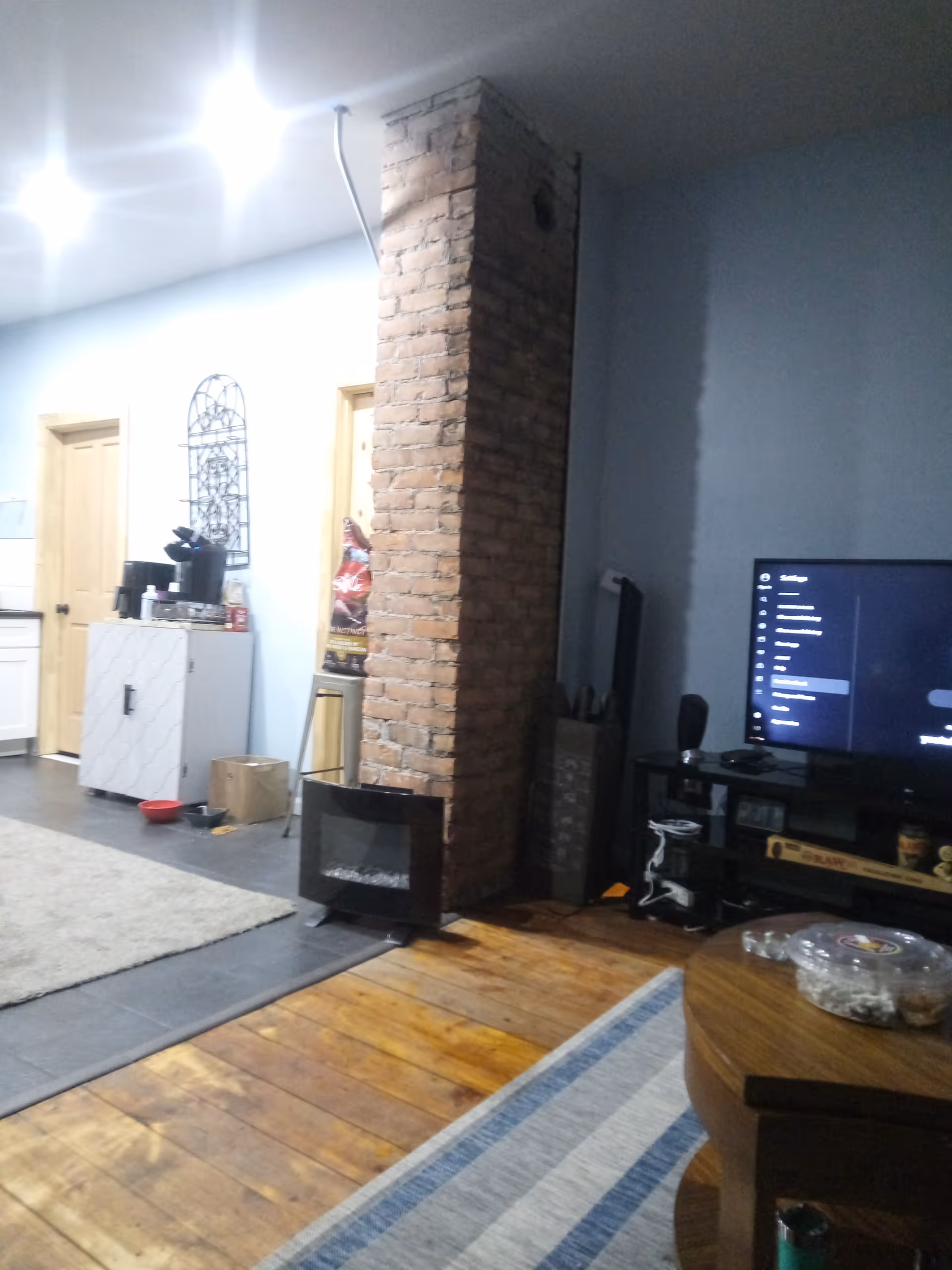 Interior living area with brick pillar, wood floors, TV, and casual seating.